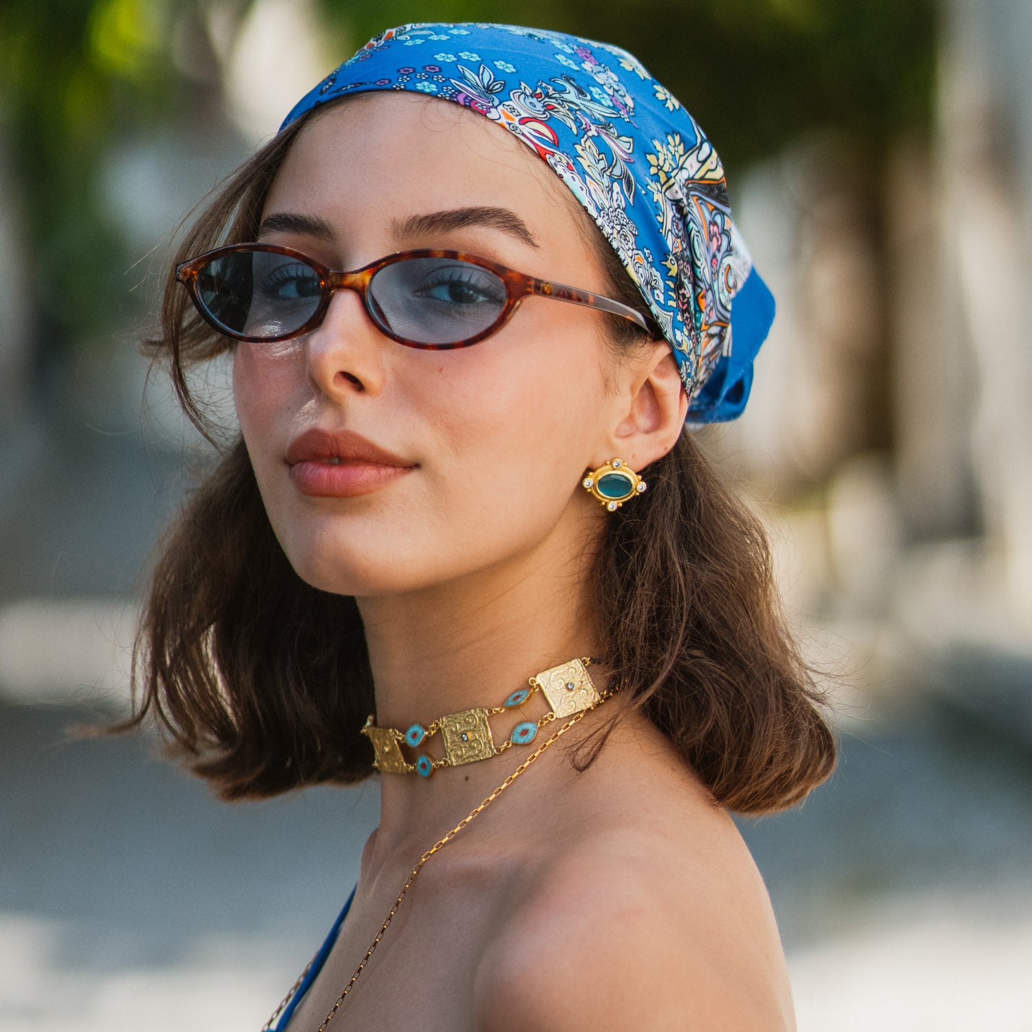 Woman in a blue headscarf and sunglasses wearing the Cleopatra Evil Eye Turquoise & Coral Engraved Gold Collar Necklace