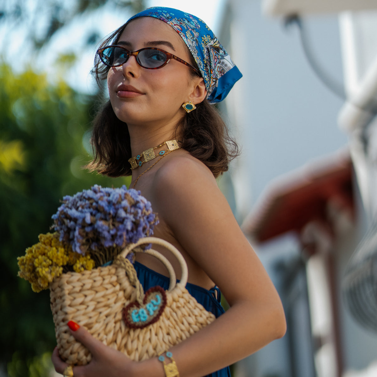 Woman holding flowers wearing the Cleopatra Evil Eye Turquoise &amp; Coral Engraved Gold Collar Necklace with matching turquoise earrings