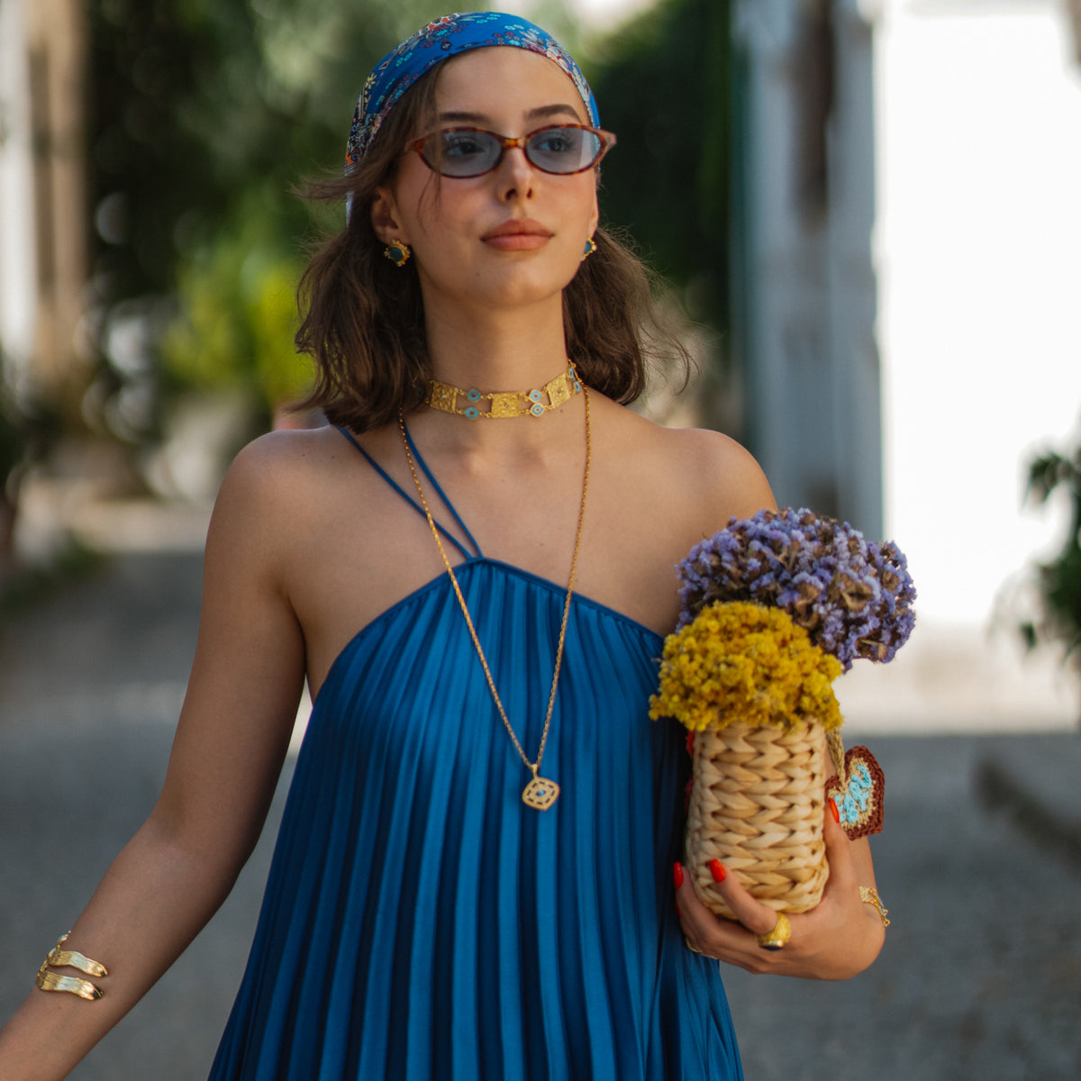 Model in a blue dress wearing the Cleopatra Evil Eye Turquoise & Coral Engraved Gold Collar Necklace with a long gold pendant