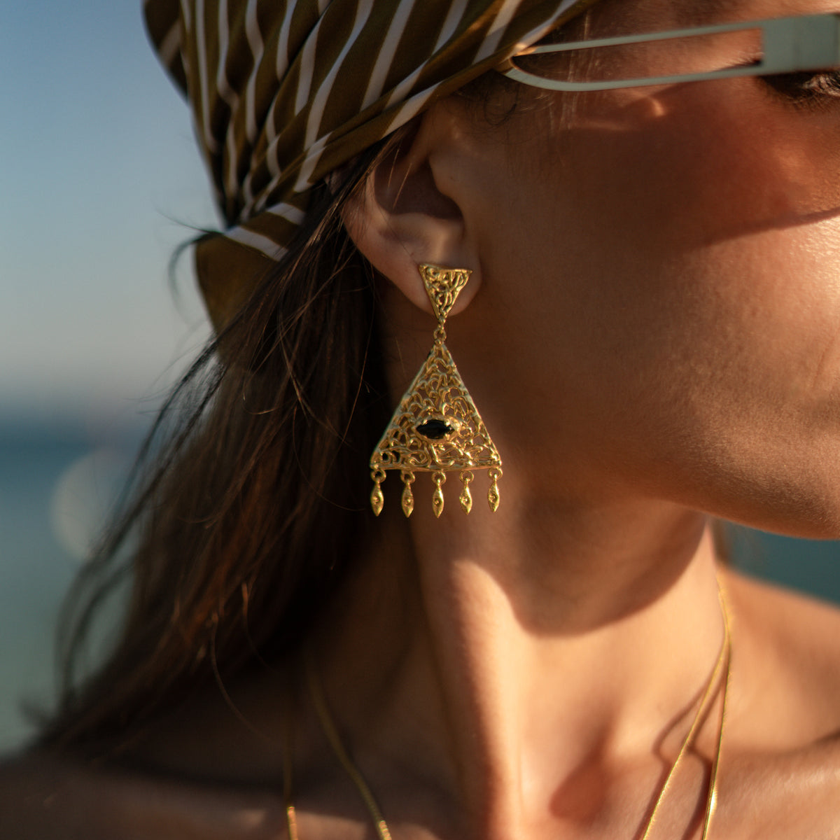 Close up of the filigree chandelier earring worn on the ear at golden hour, the black onyx dark against the openwork gold