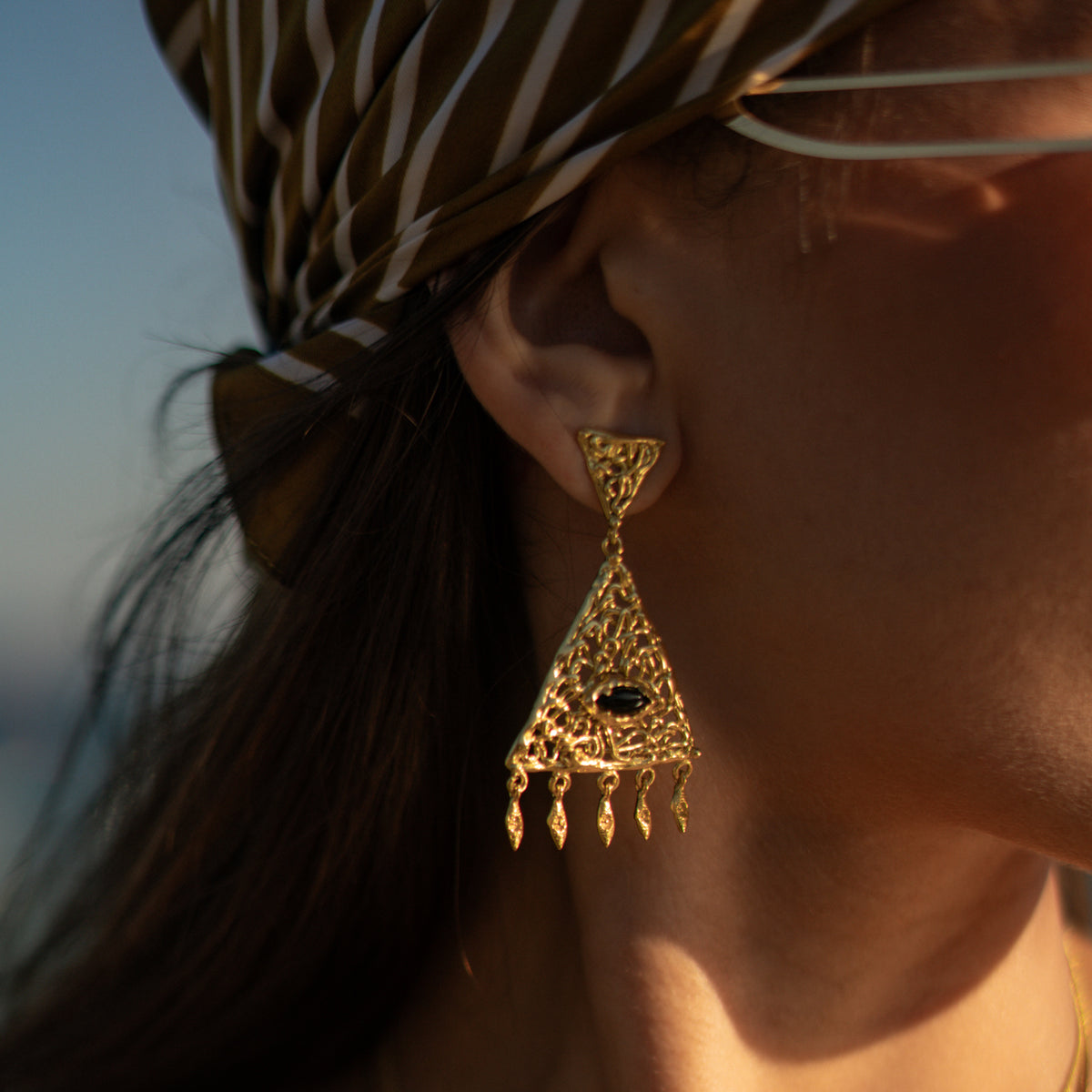 The filigree chandelier earring in profile against the ear, showing the small triangular stud and the five swinging drops