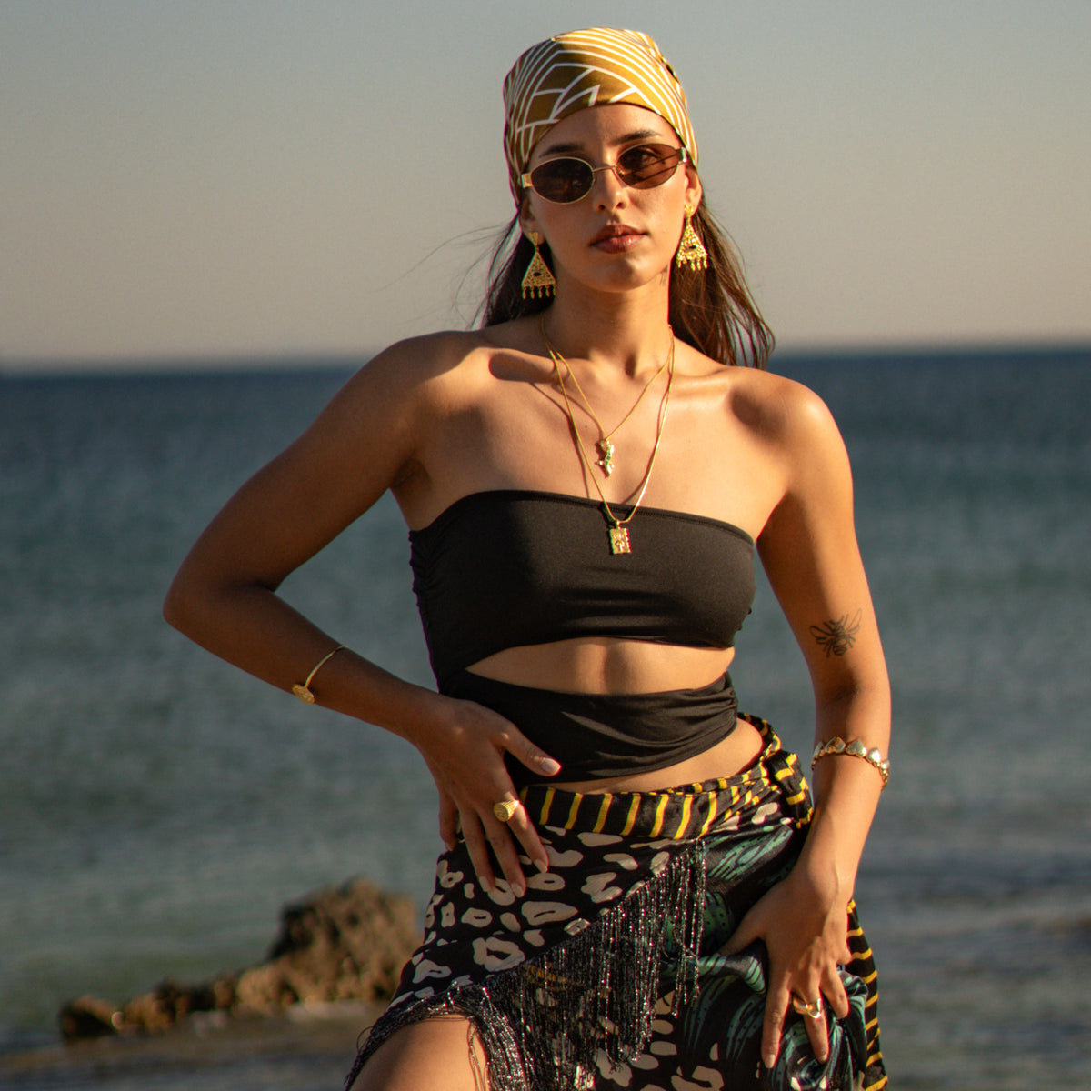 Model on the shoreline wearing the Cleopatra filigree black onyx chandelier earrings with a printed headscarf