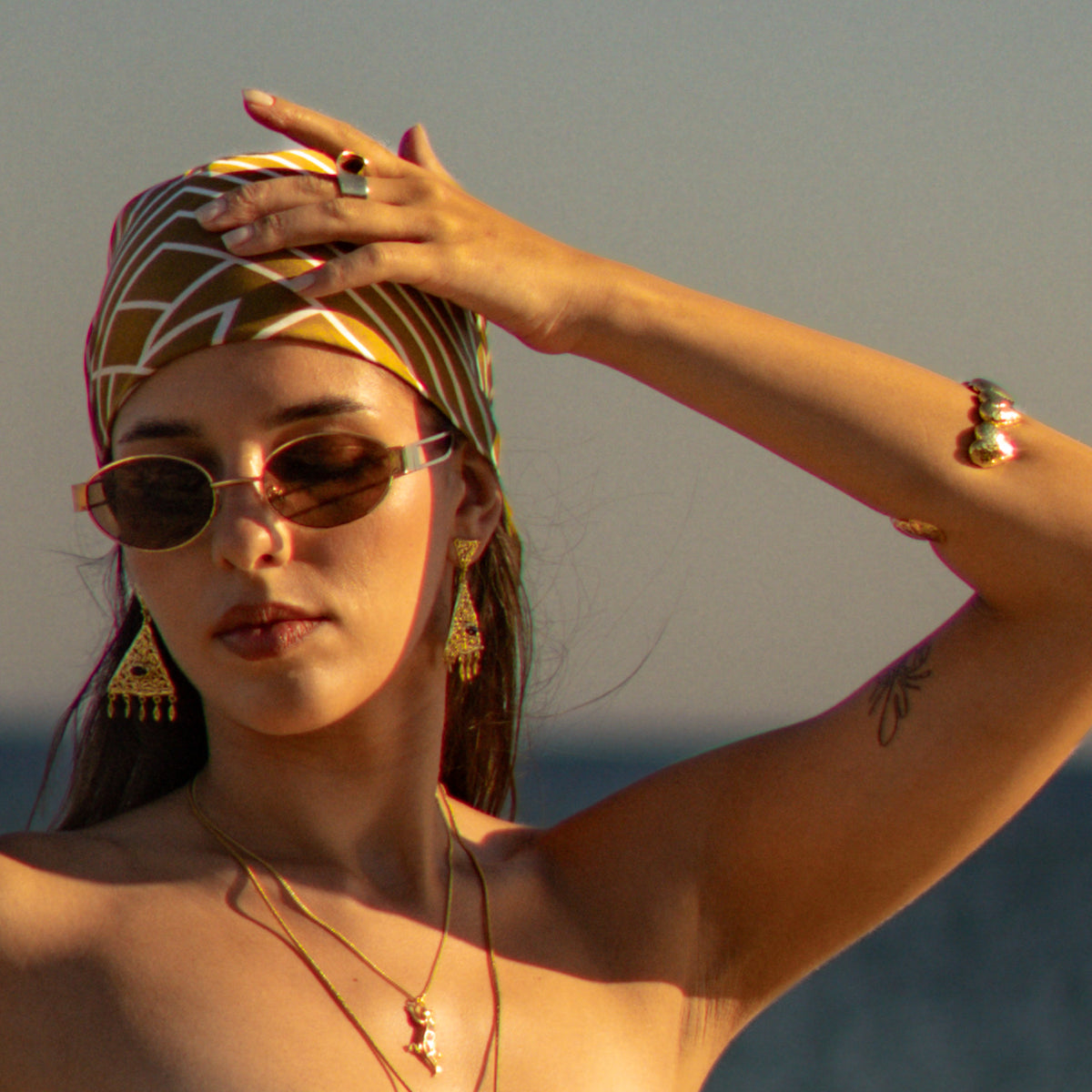 Woman with her hand raised to her headscarf, the gold filigree chandelier earrings catching the evening light