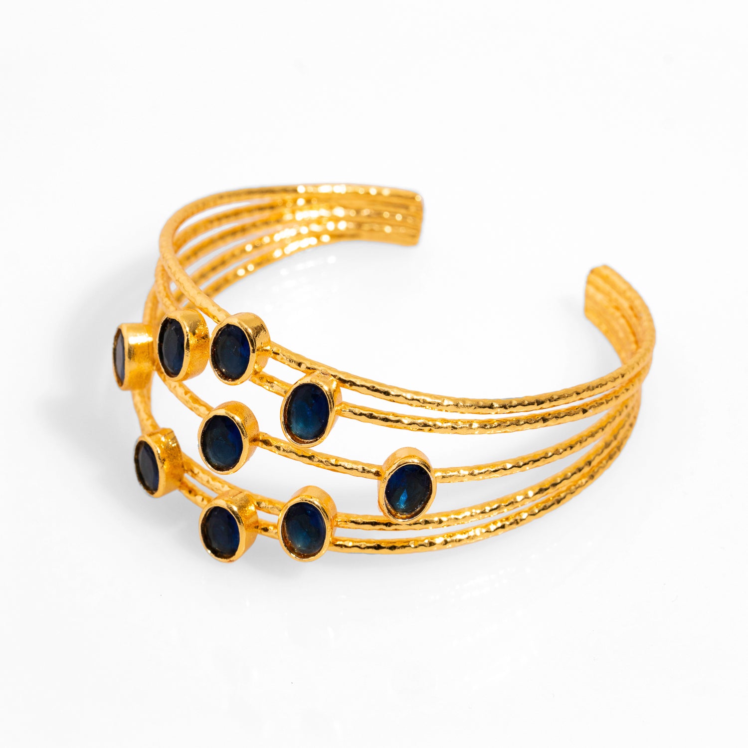 Chunky cuff bracelet with 24k gold plating and five thin gold wires, adorned with oval sapphire stones, adjustable size.
