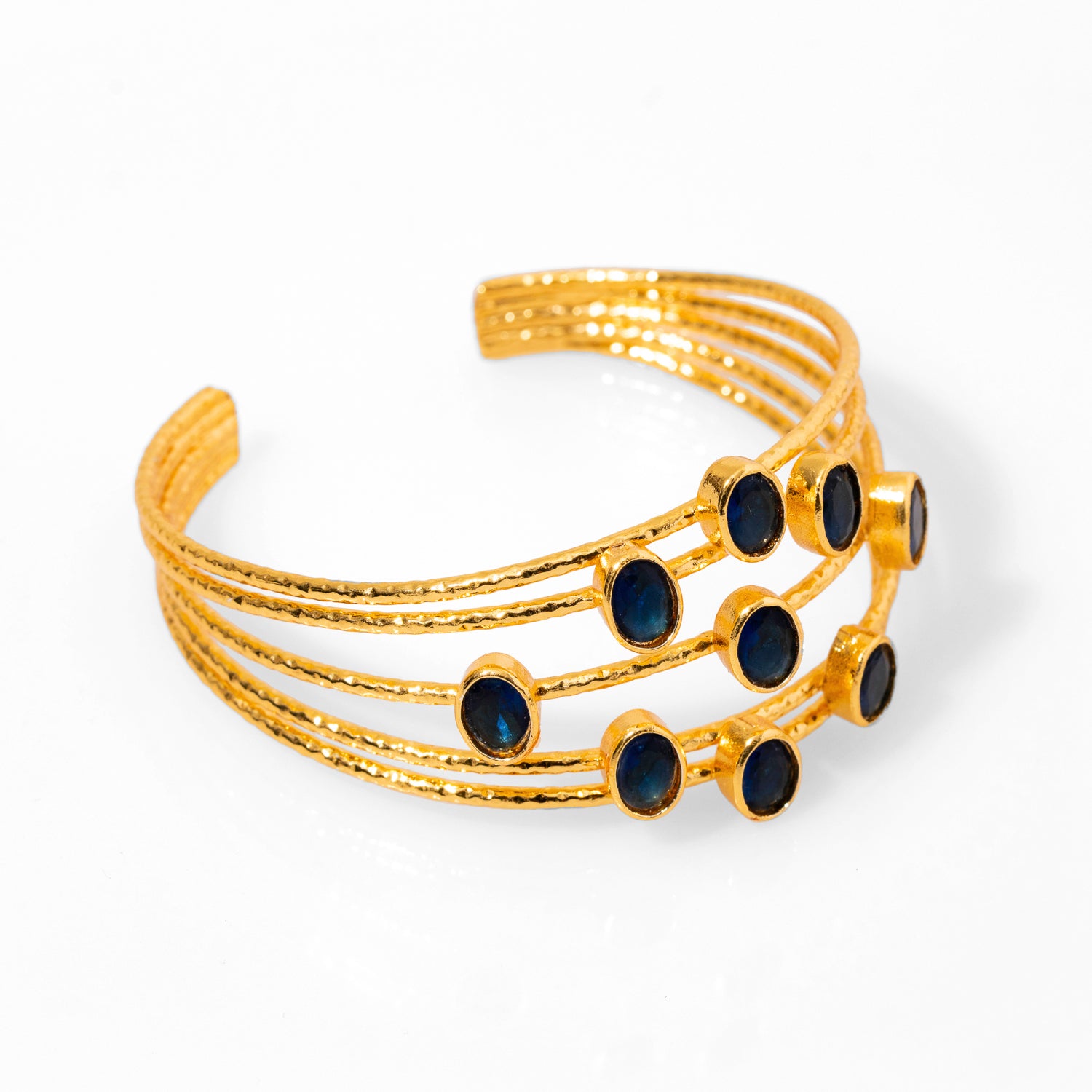 Sophisticated chunky cuff bracelet with 24k gold plating and sapphire stones, designed with five gold wires, adjustable fit.
