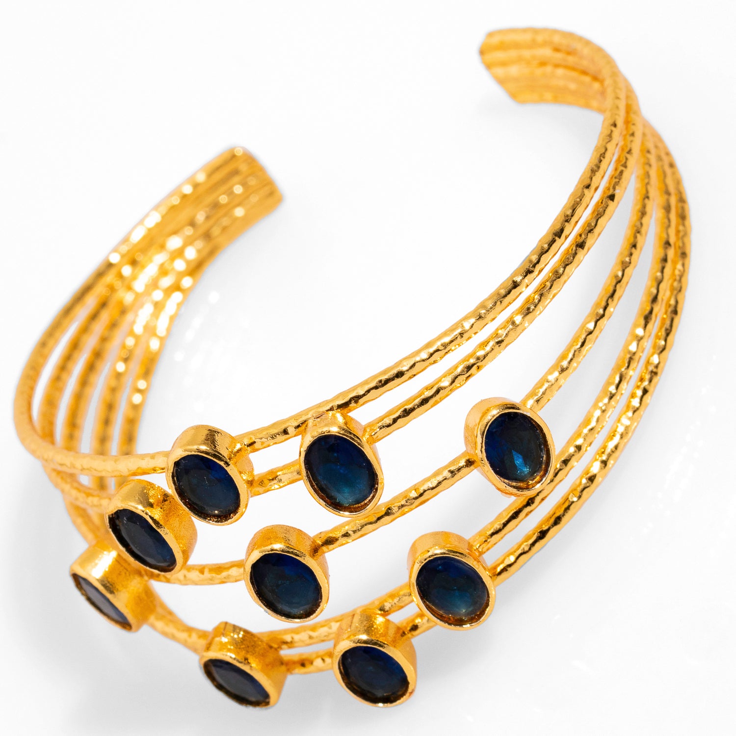 24k gold-plated chunky cuff bracelet with five gold wires and oval sapphire stones, offering a sophisticated and adjustable fit.
