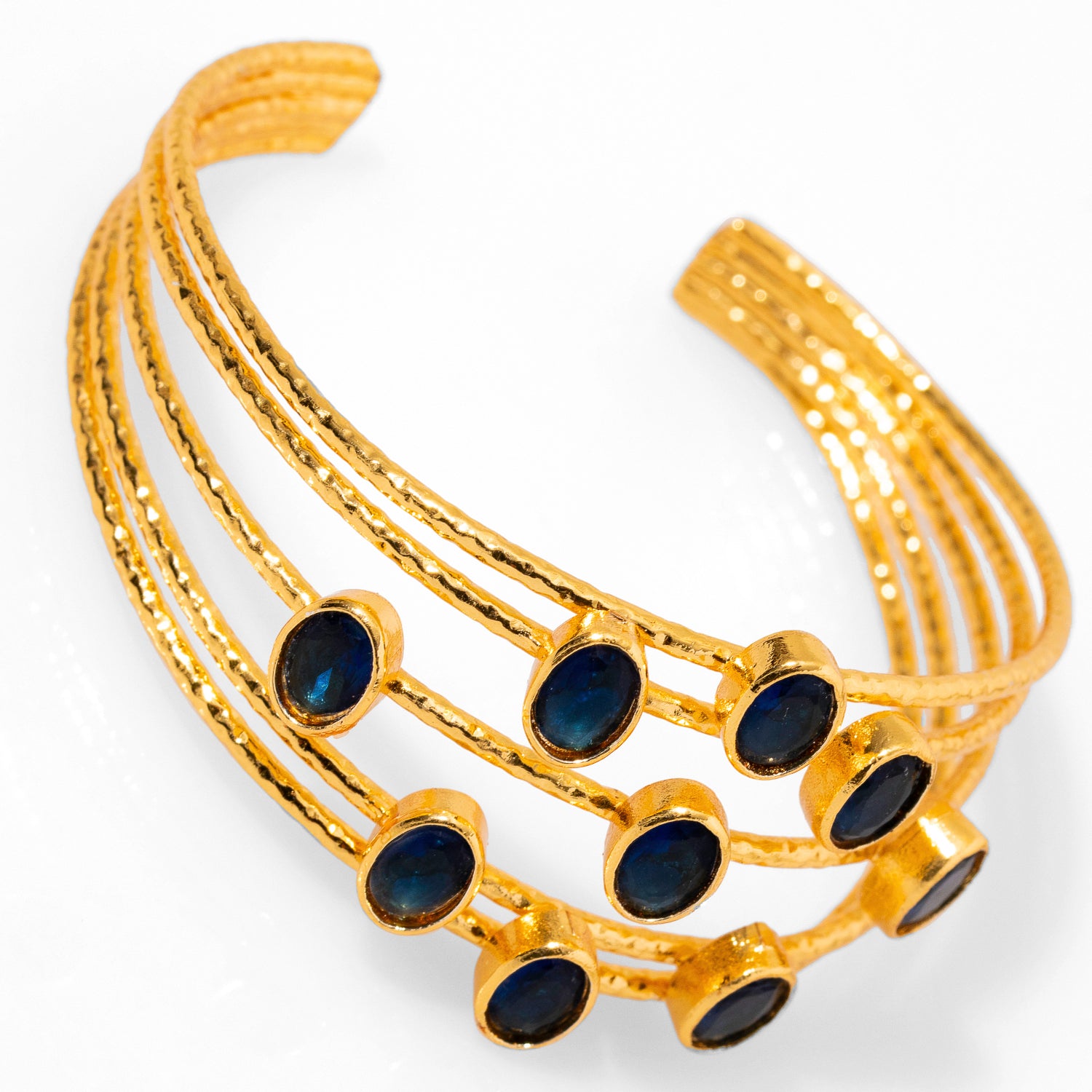 Refined gold cuff bracelet with 24k plating, incorporating oval sapphire stones and five gold wires, adjustable for a perfect fit.
