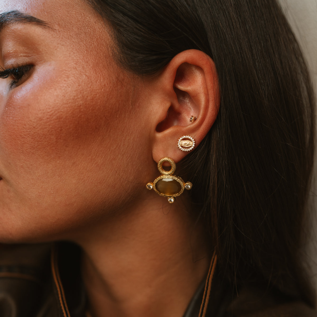 Close view of the Cleopatra Golden Citrine earring on the ear, the cat eye stone glowing amber, with a small evil eye stud above