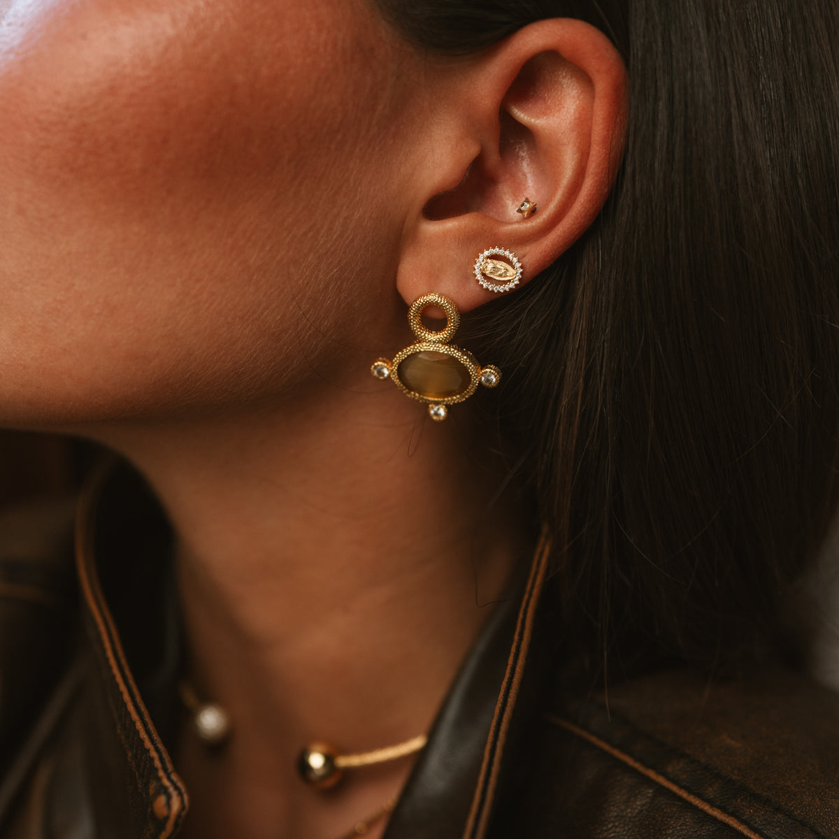 Profile close-up of the Cleopatra Golden Citrine cat eye earring worn with a gold and pearl open choker