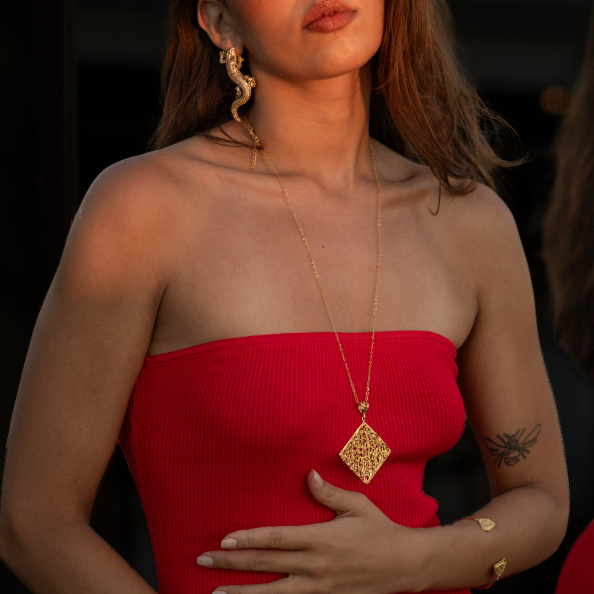 Cleopatra Golden Lace Long Pendant Necklace worn over a red dress, gold lace panel resting mid chest