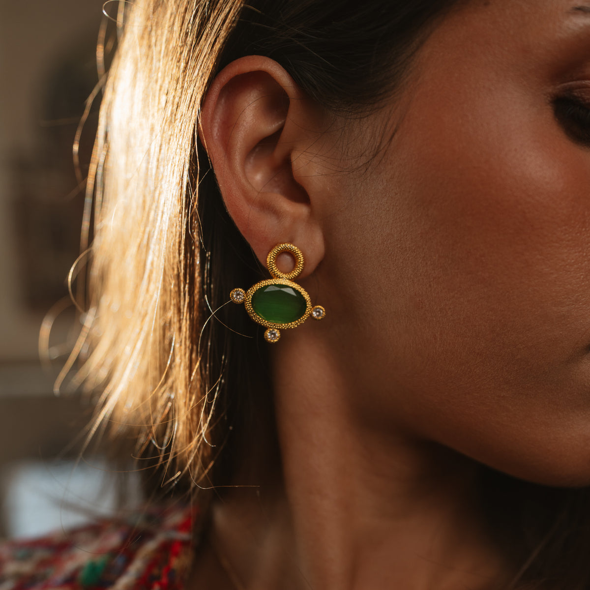 Close up of the Cleopatra Green Cat Eye gold stud earring worn on the ear in warm light