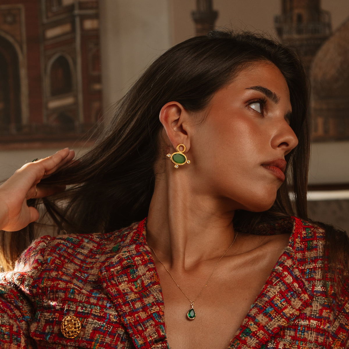 Model in a red tweed jacket wearing the Cleopatra Green Cat Eye gold stud earring with a green teardrop pendant