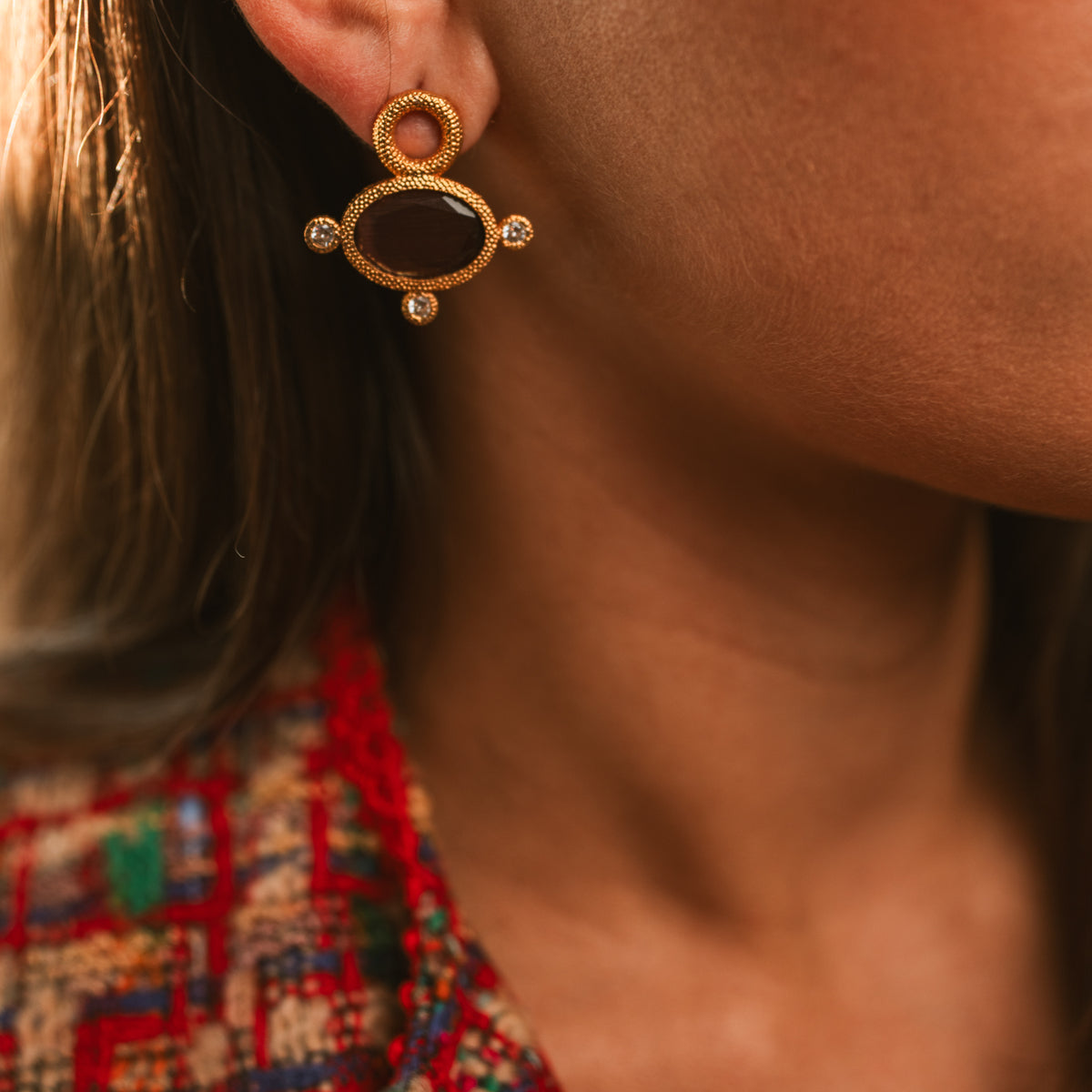 Cleopatra Mocha cat eye earring on the ear above a red tweed jacket, the stone nearly black in shade