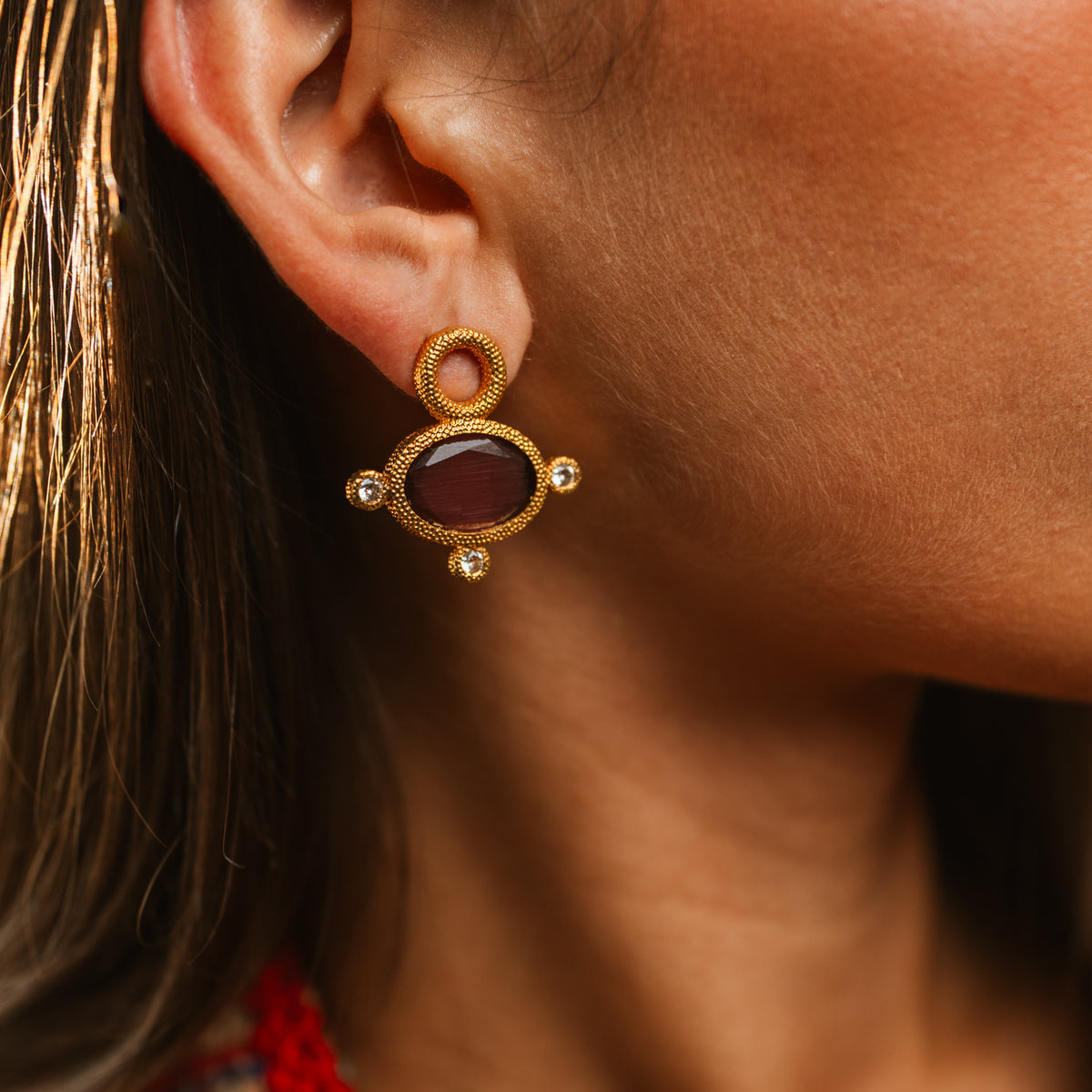 Cleopatra Mocha cat eye gold earring worn on the ear, the stone glowing dark chocolate in sunlight