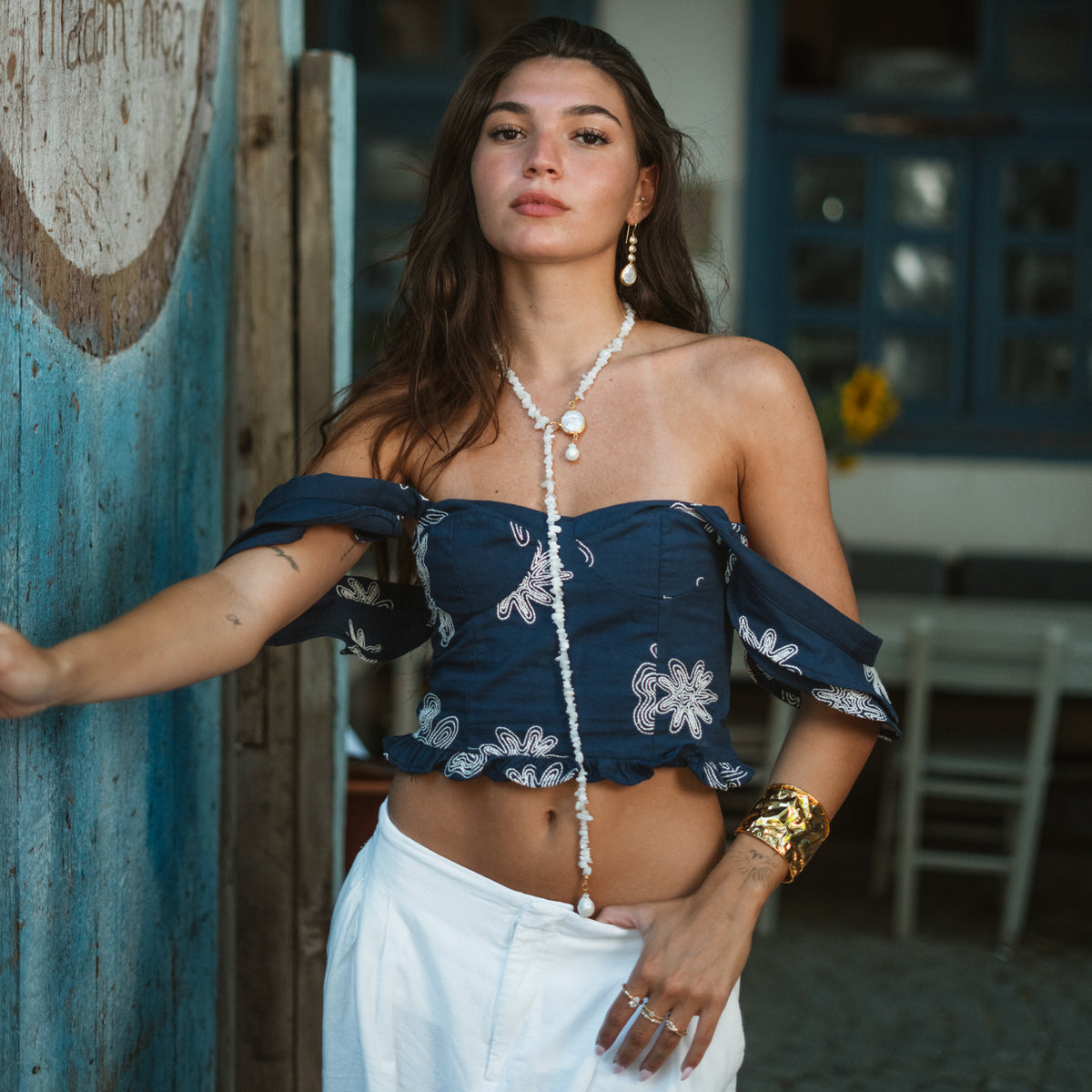 Model in a navy off the shoulder top and white trousers wearing the pearl cascade gold drop earrings with a long white beaded lariat