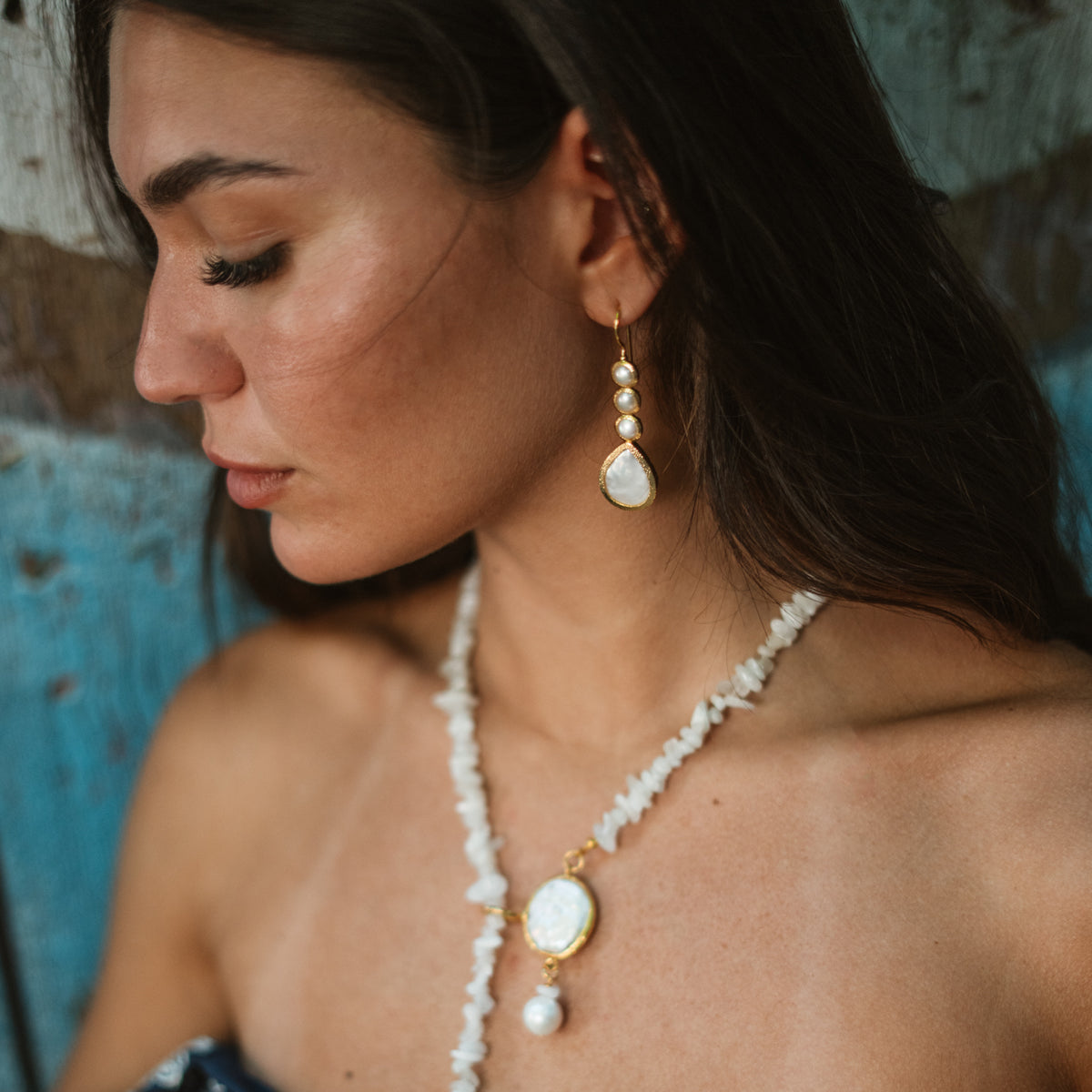 Model looking down in profile wearing the Cleopatra pearl cascade earring with a long white beaded necklace and pearl pendant