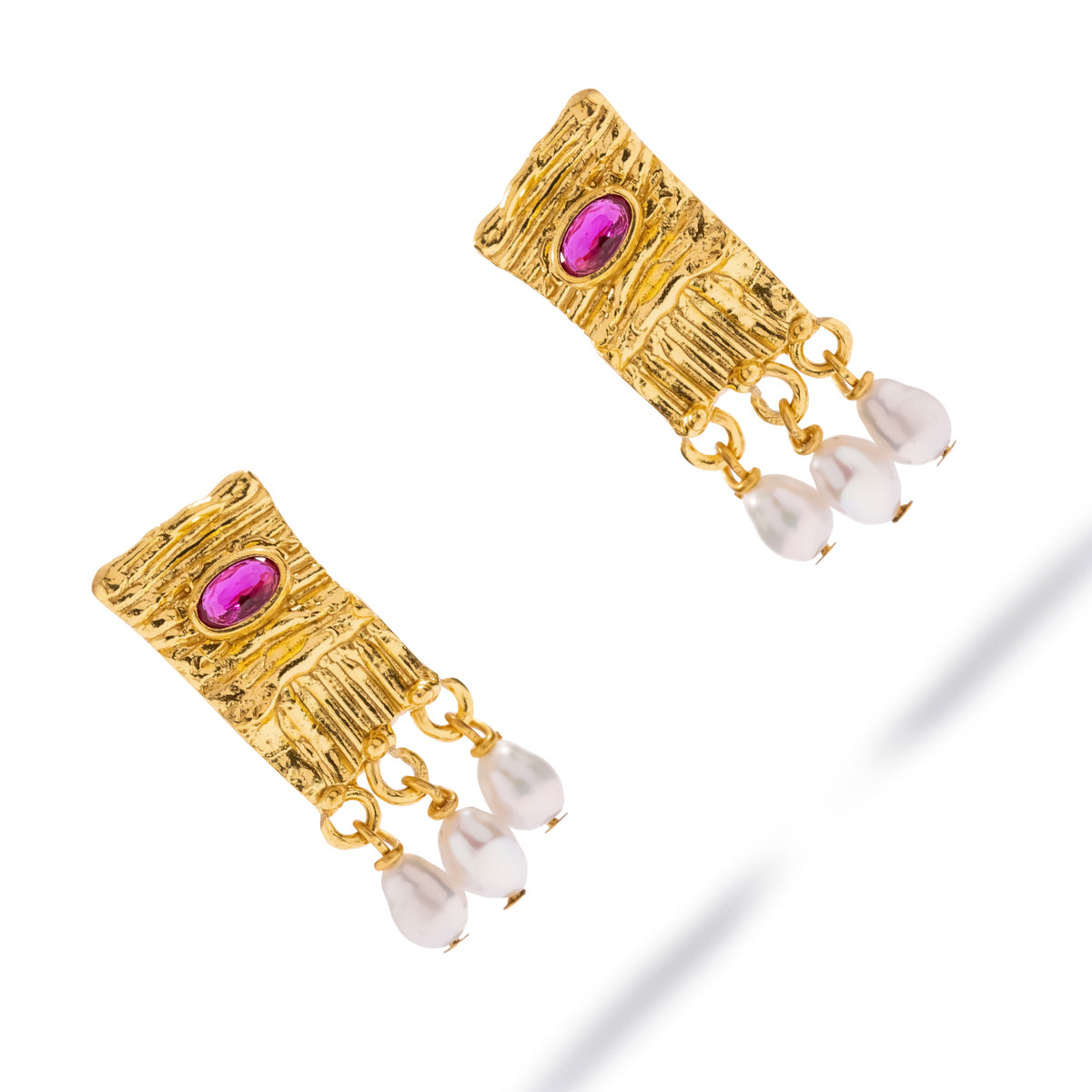 Cleopatra ruby and pearl gold tablet earrings laid diagonally on white