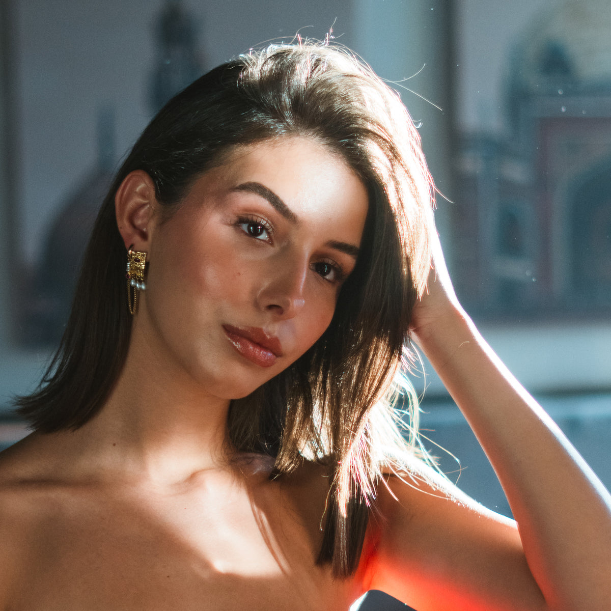 Model with a hand in her hair wearing the Cleopatra Ruby & Pearl Gold Statement Earrings