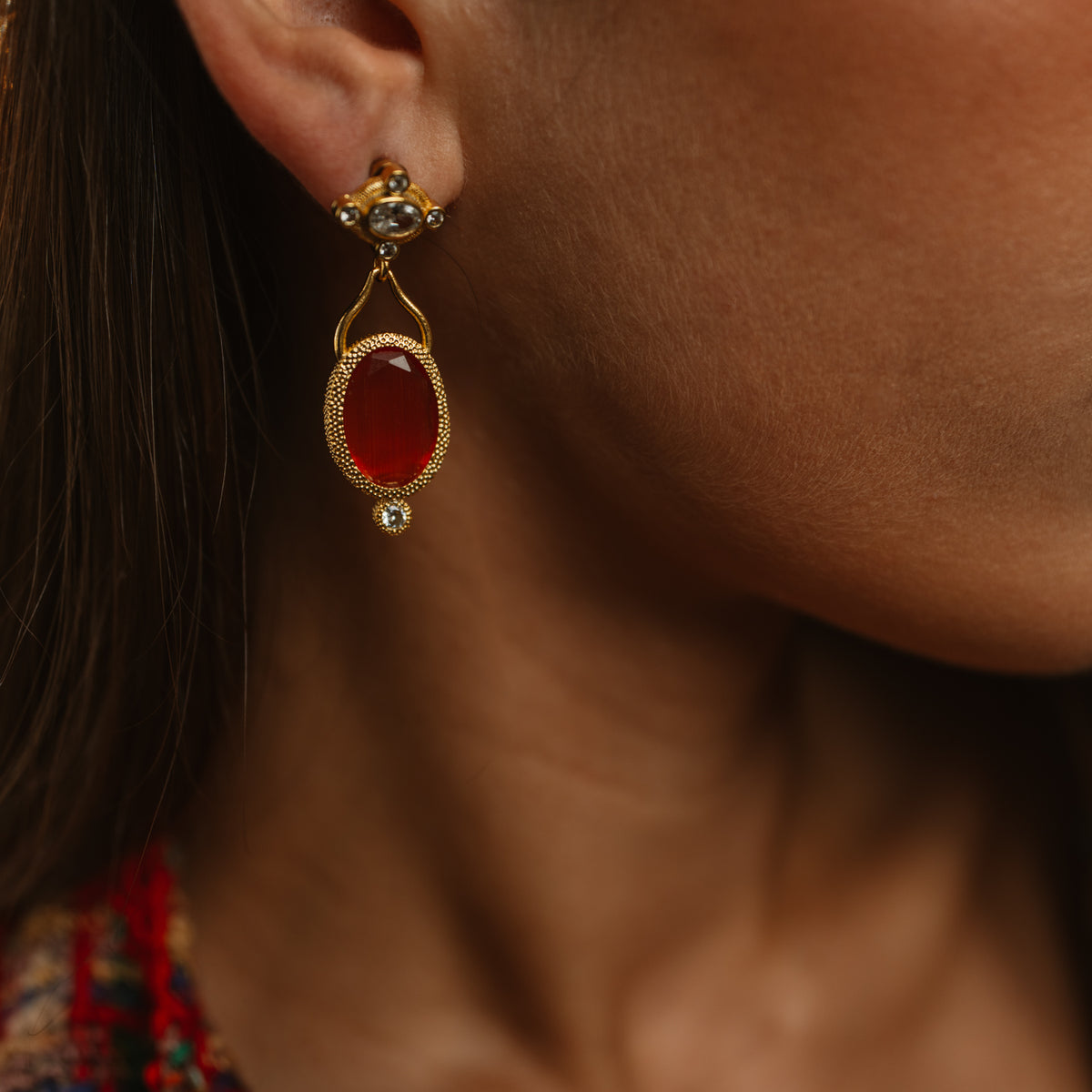 Close view of the Cleopatra Sunset drop earring on the ear, the cat eye stone glowing deep red in warm light