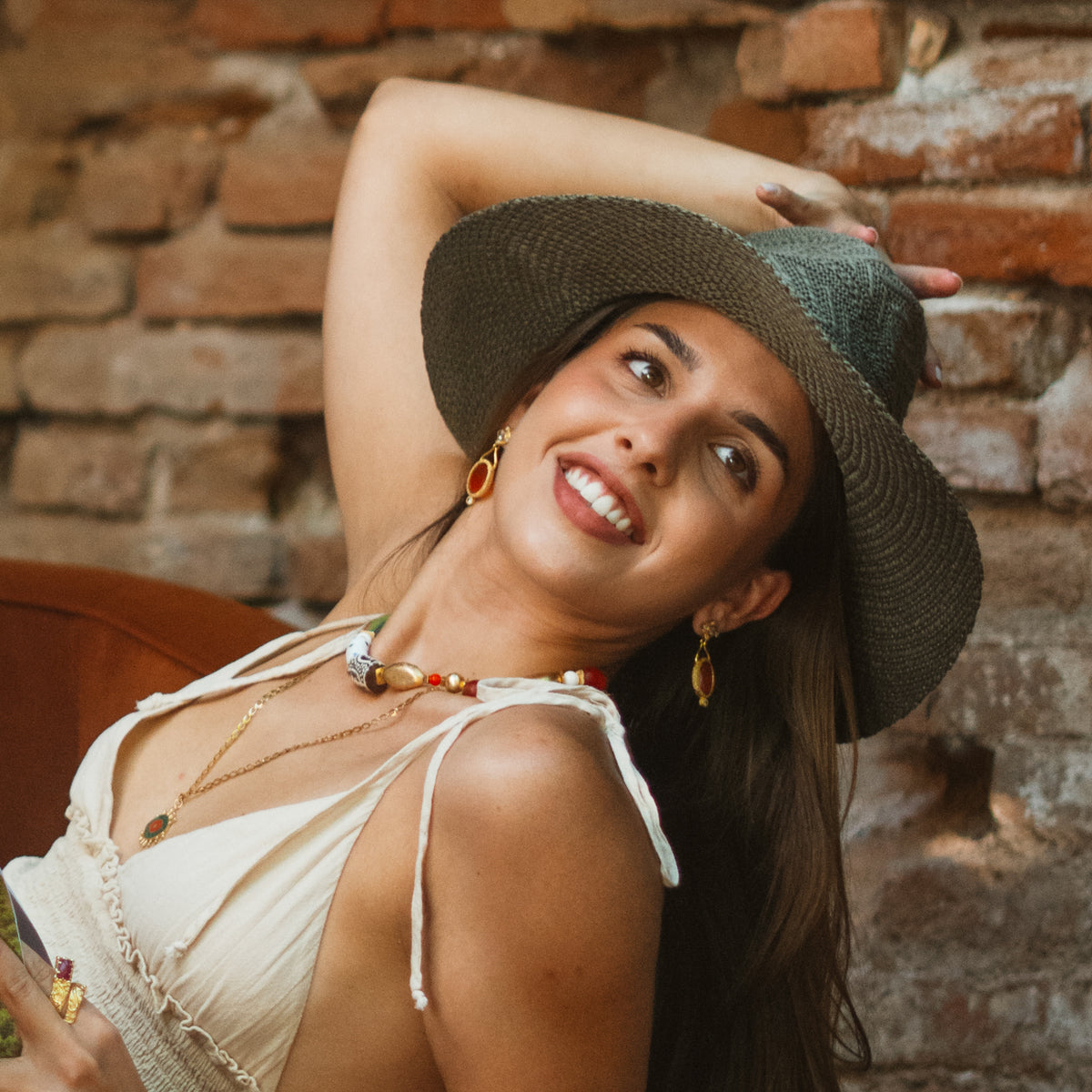 Smiling model in a green straw hat and white top wearing the Cleopatra Sunset cat eye gold drop earrings