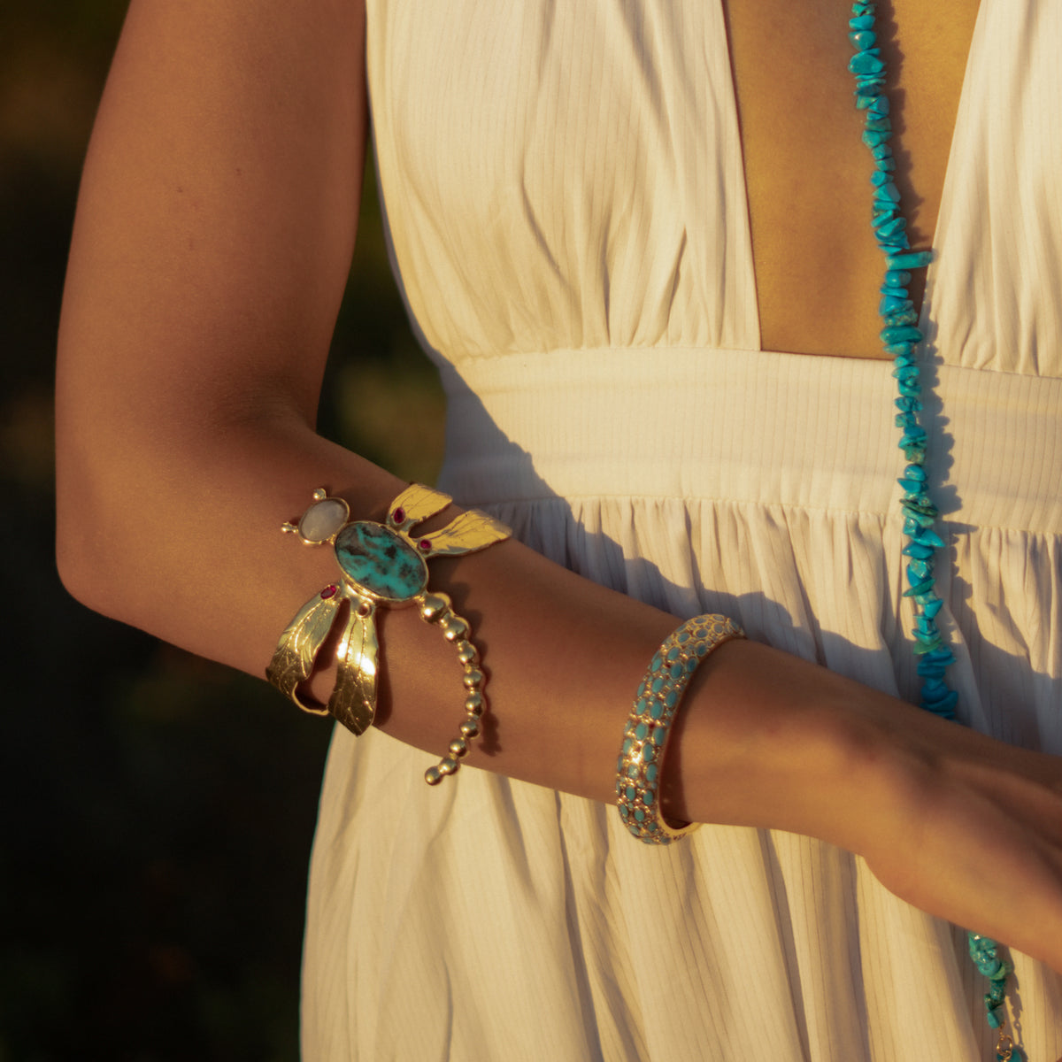 Woman in a white dress wearing the Cleopatra turquoise bangle with a gold armlet and a long turquoise necklace