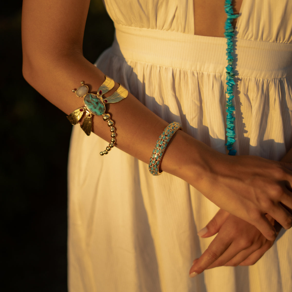 Turquoise and gold bangle on a woman's wrist in warm evening light, styled with a white dress