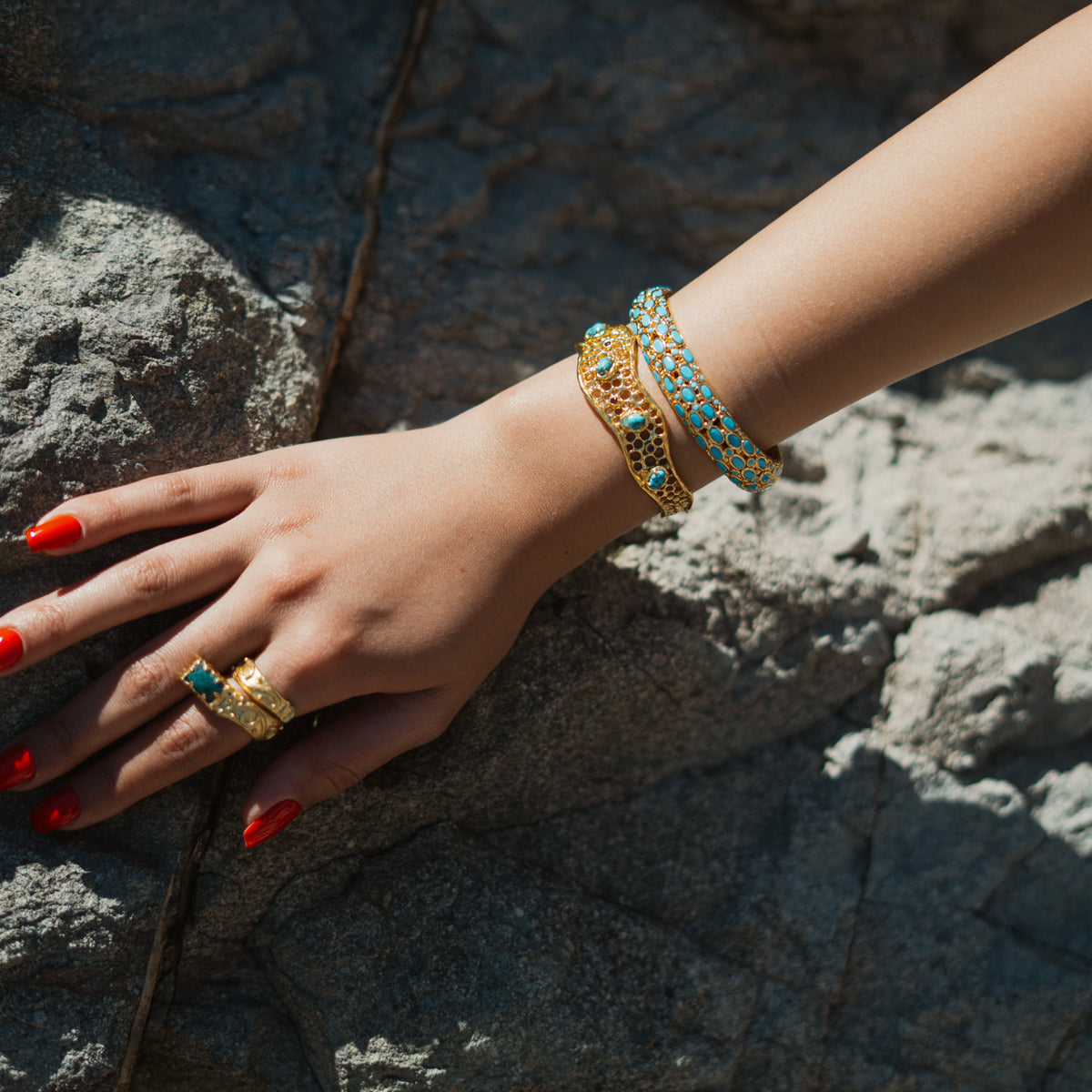 Hand resting on sunlit rock wearing the turquoise cabochon gold bangle stacked with a gold cuff and stone rings
