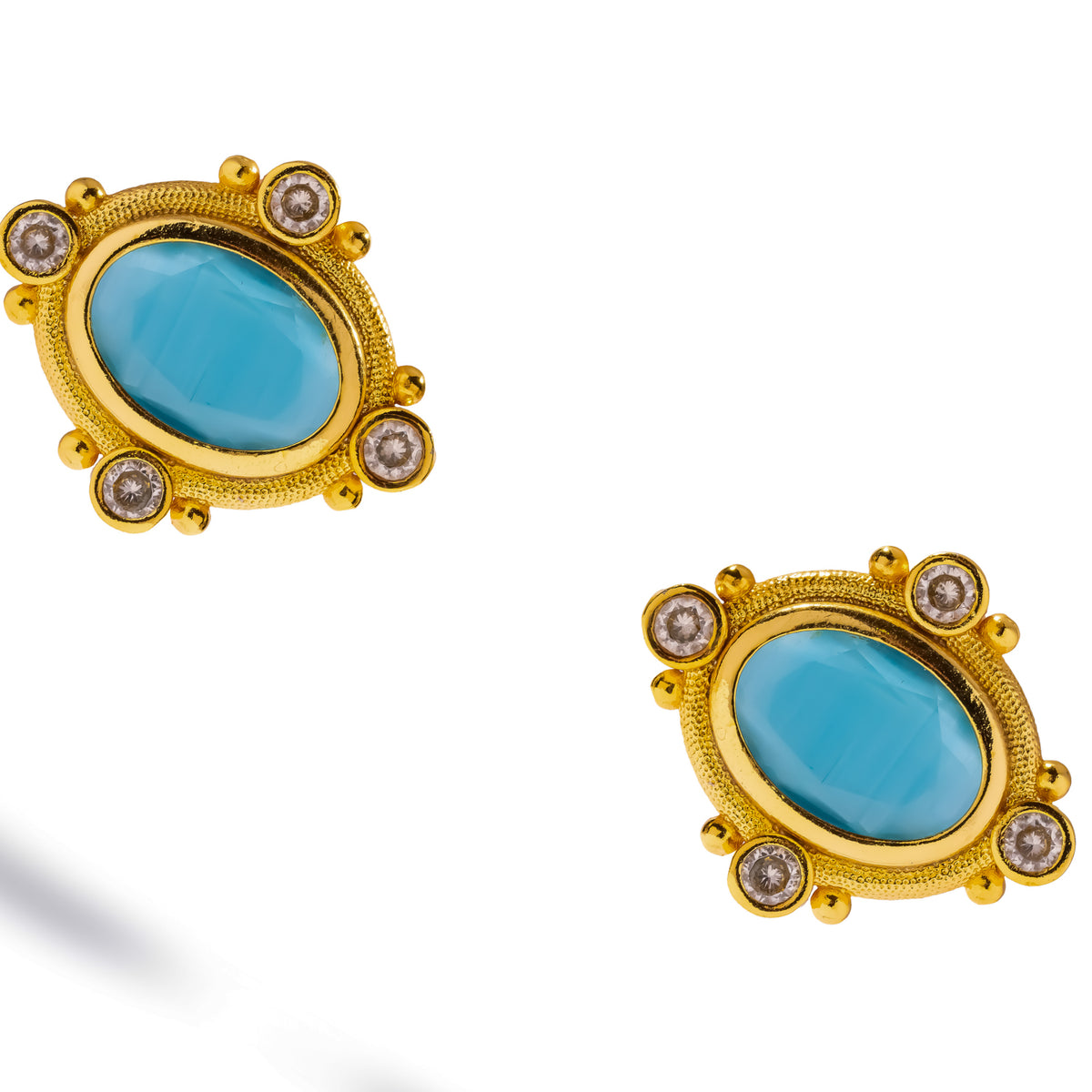Pair of Cleopatra Turquoise cat eye studs at an angle, clear accents and gold beads around each oval stone