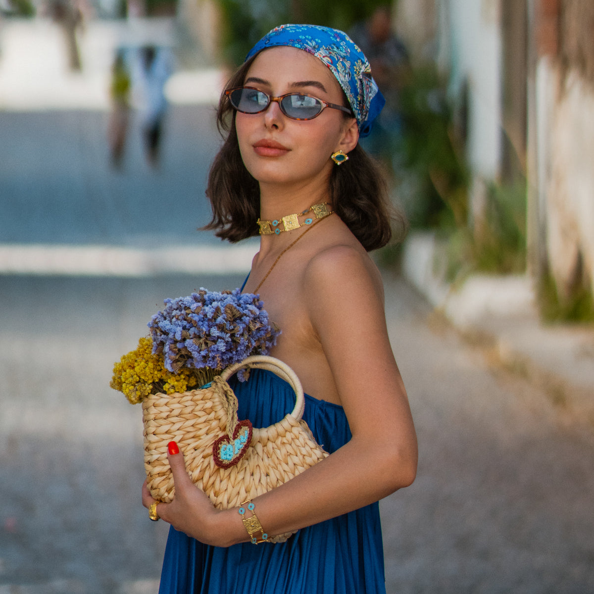 Model on a village street with a straw basket of dried flowers, wearing the Cleopatra Turquoise cat eye gold studs
