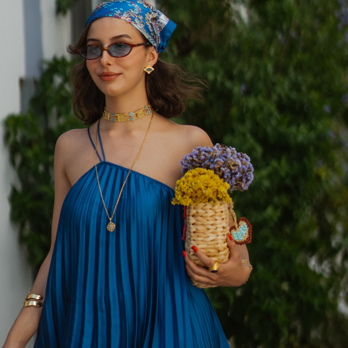 Model walking in a blue pleated dress and headscarf, the Cleopatra Turquoise stud earrings catching the light