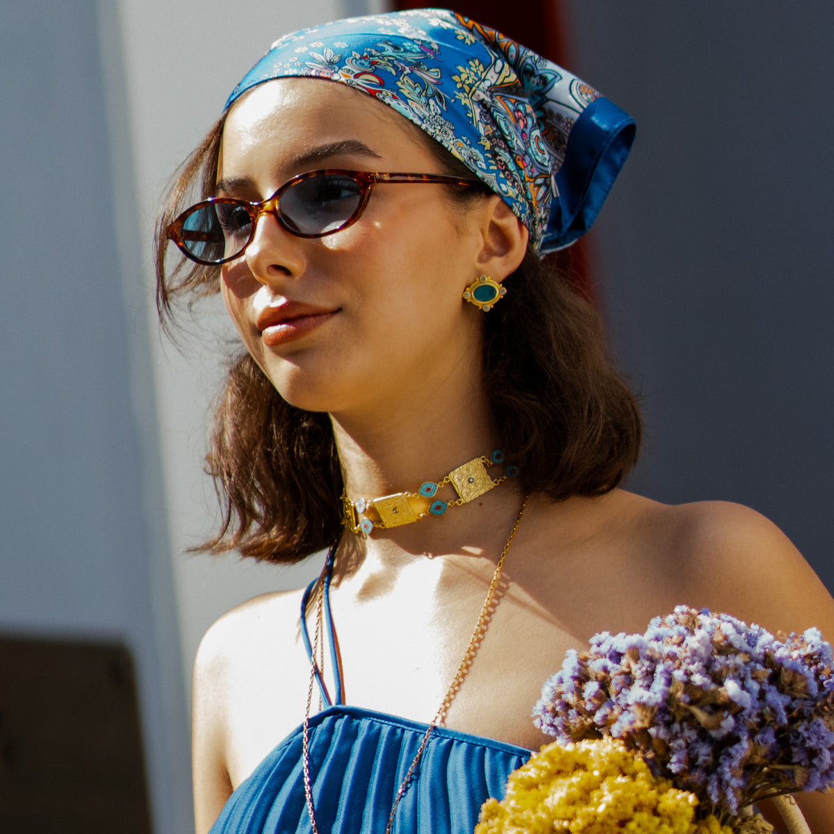 Sunlit portrait in a blue headscarf, the Cleopatra Turquoise cat eye gold stud earring with a gold evil eye choker