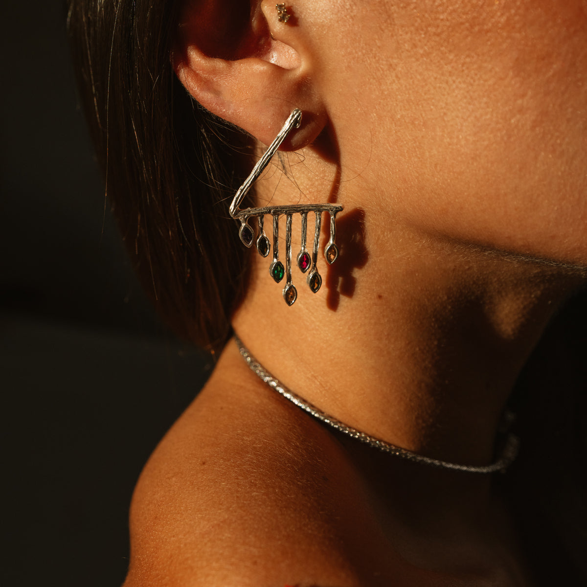 Close side view of the Color Rhythm silver earring on the model, violet, green and magenta stones catching the light