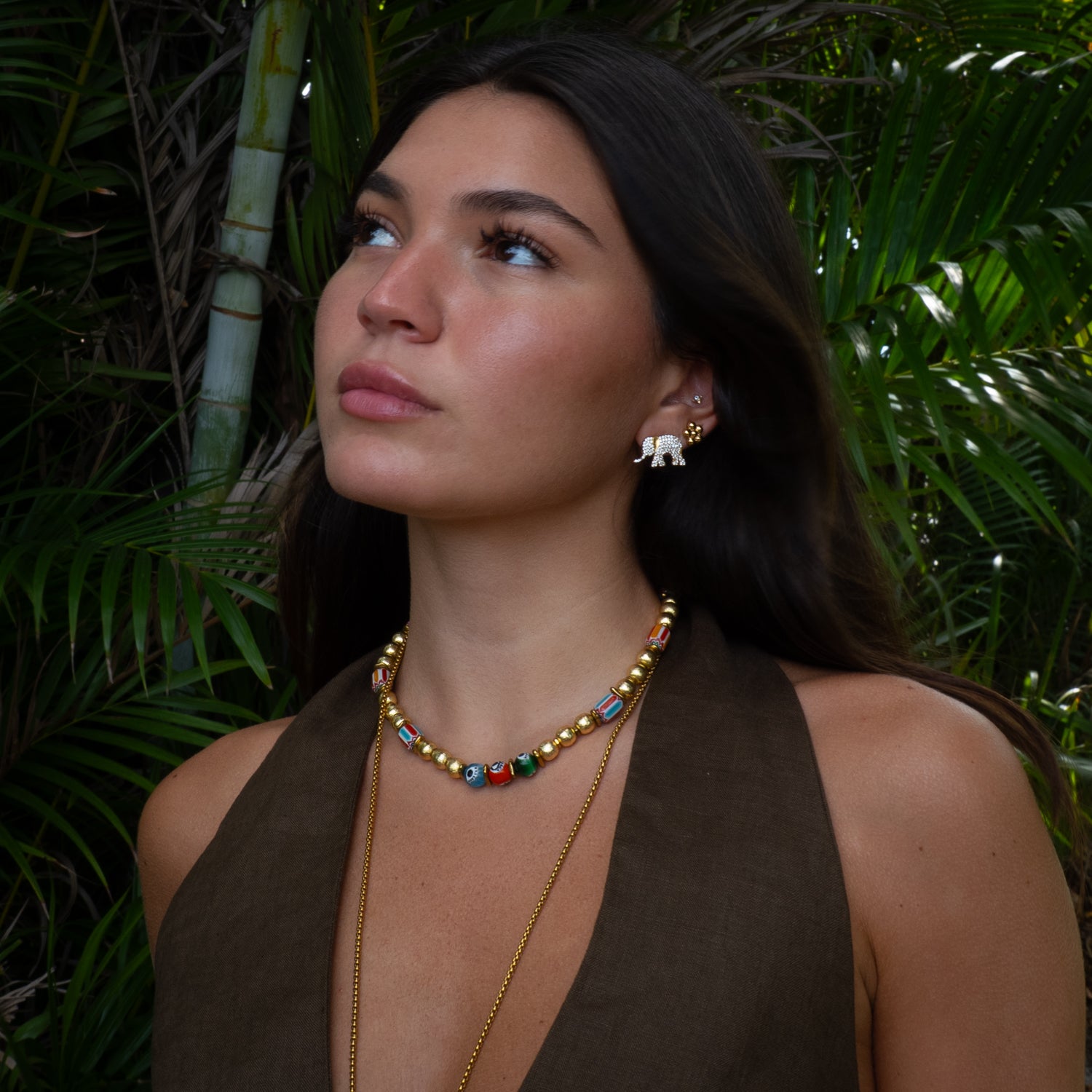 Woman wearing a colorful necklace and earrings with a green leafy background
