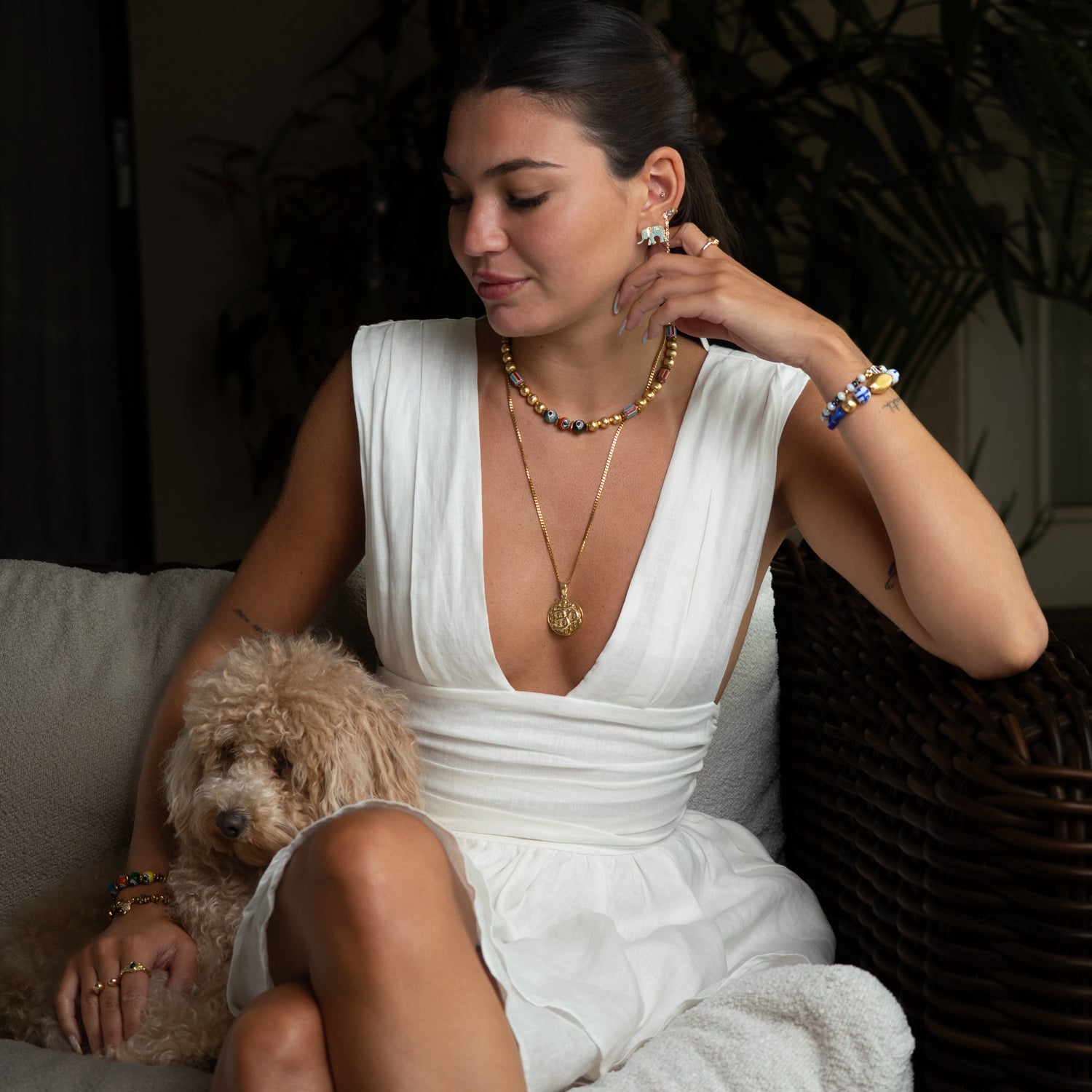 Woman in a white dress sitting on a couch with a dog, wearing jewelry.