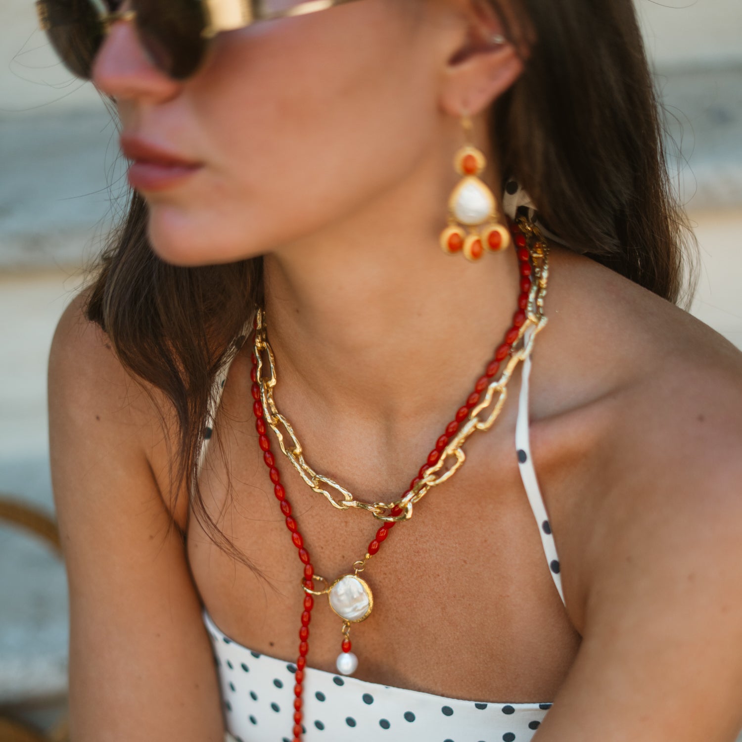 Close-up of the coral pearl lariat necklace layered with a gold chain necklace, worn with matching coral pearl earrings