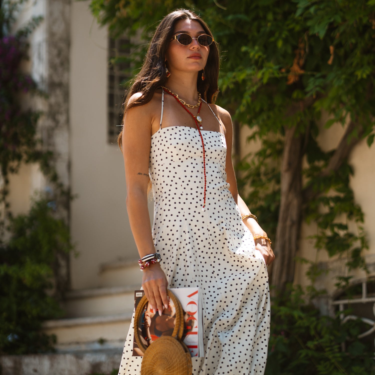 Model wearing the handmade coral vitality pearl lariat necklace with a polka dot dress, holding a straw hat and Vogue magazine