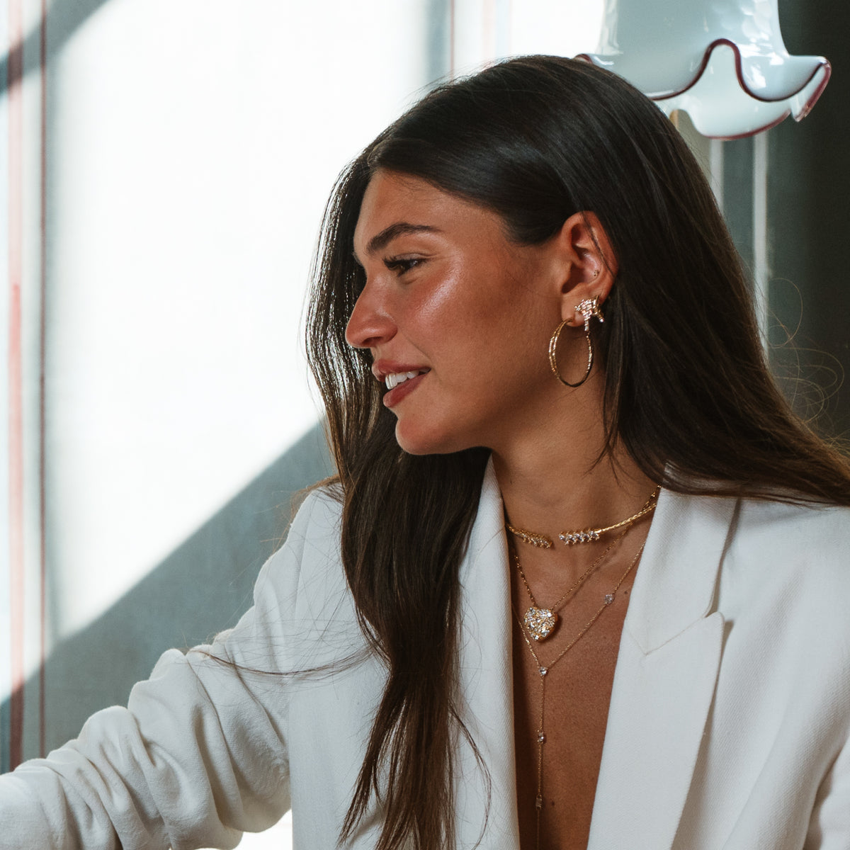 Model in profile by a sunlit window, smiling, wearing the shooting star stud earring with a layered choker and pendant necklaces