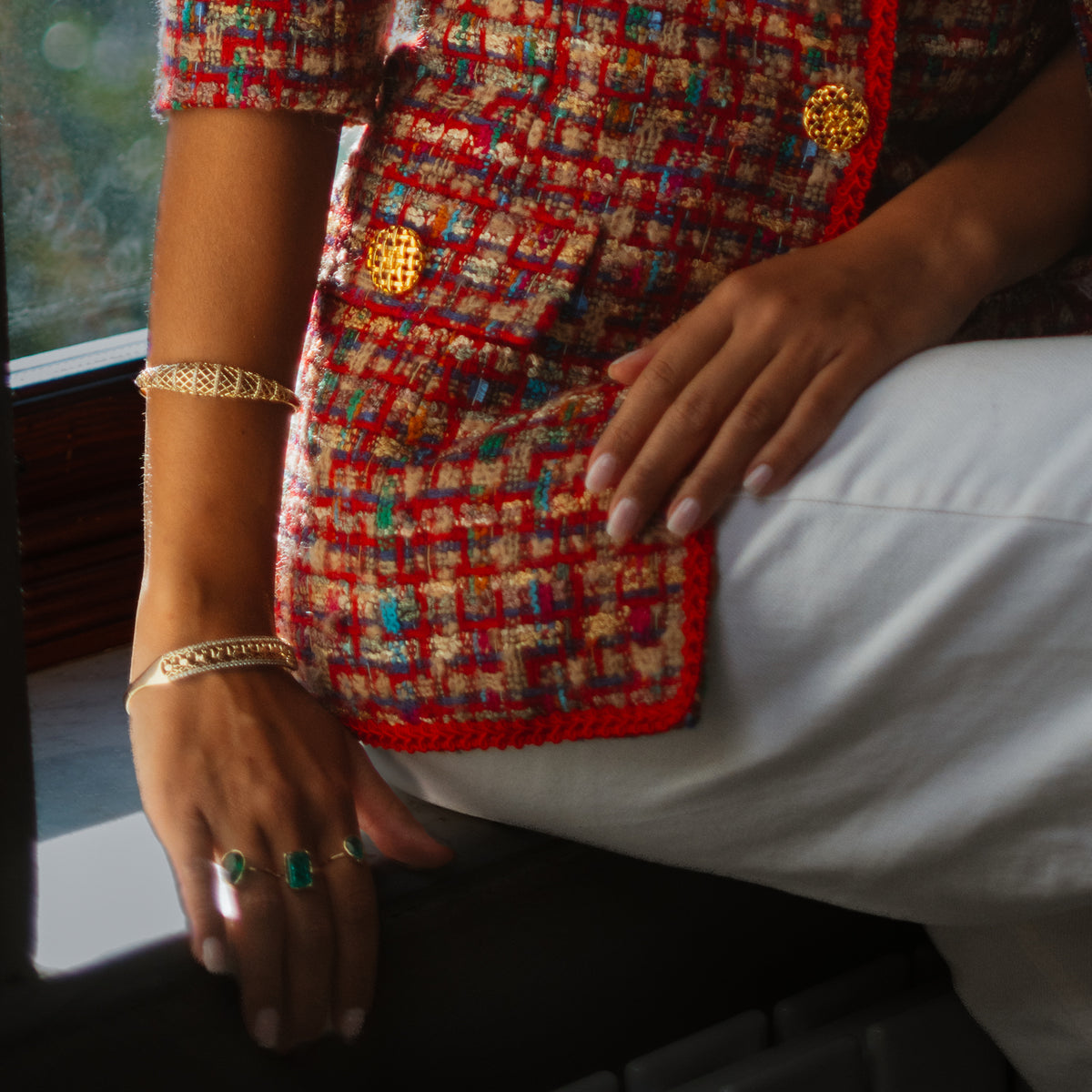 Seated woman in a red tweed jacket wearing gold bangles on both wrists
