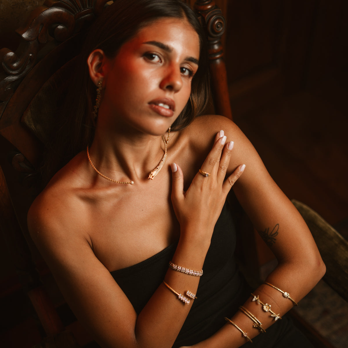 Model seated in warm light wearing the gold panther collar necklace and gold bangles
