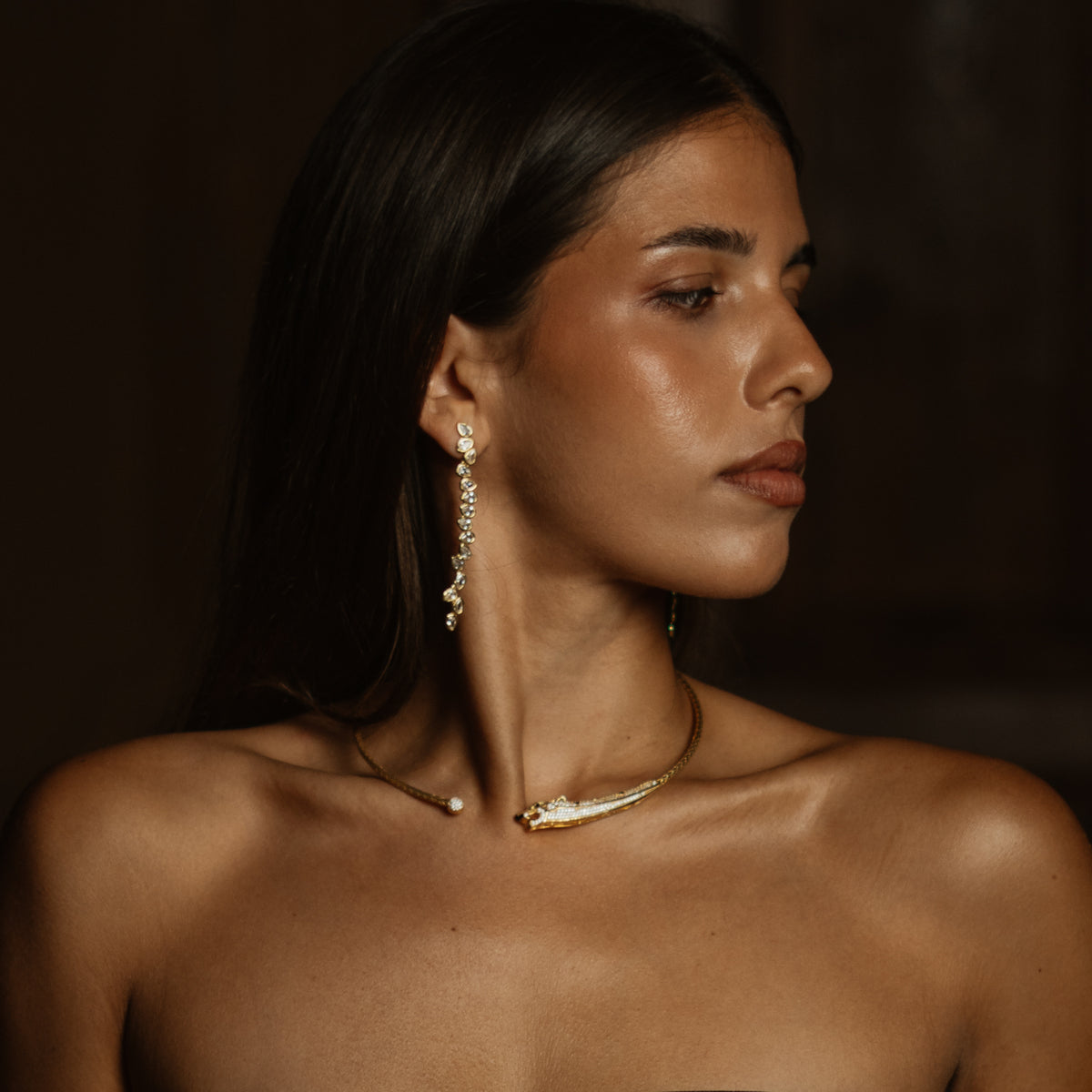 Model in warm low light wearing the chic diamond vine gold earrings and a gold collar necklace