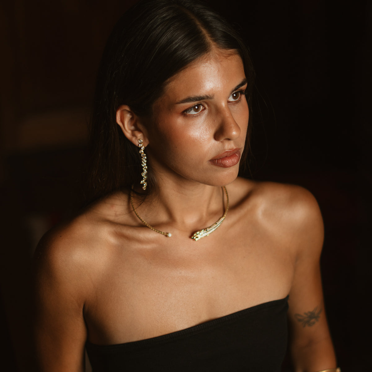 Woman in a black strapless top wearing the long gold vine drop earrings with a gold panther collar necklace