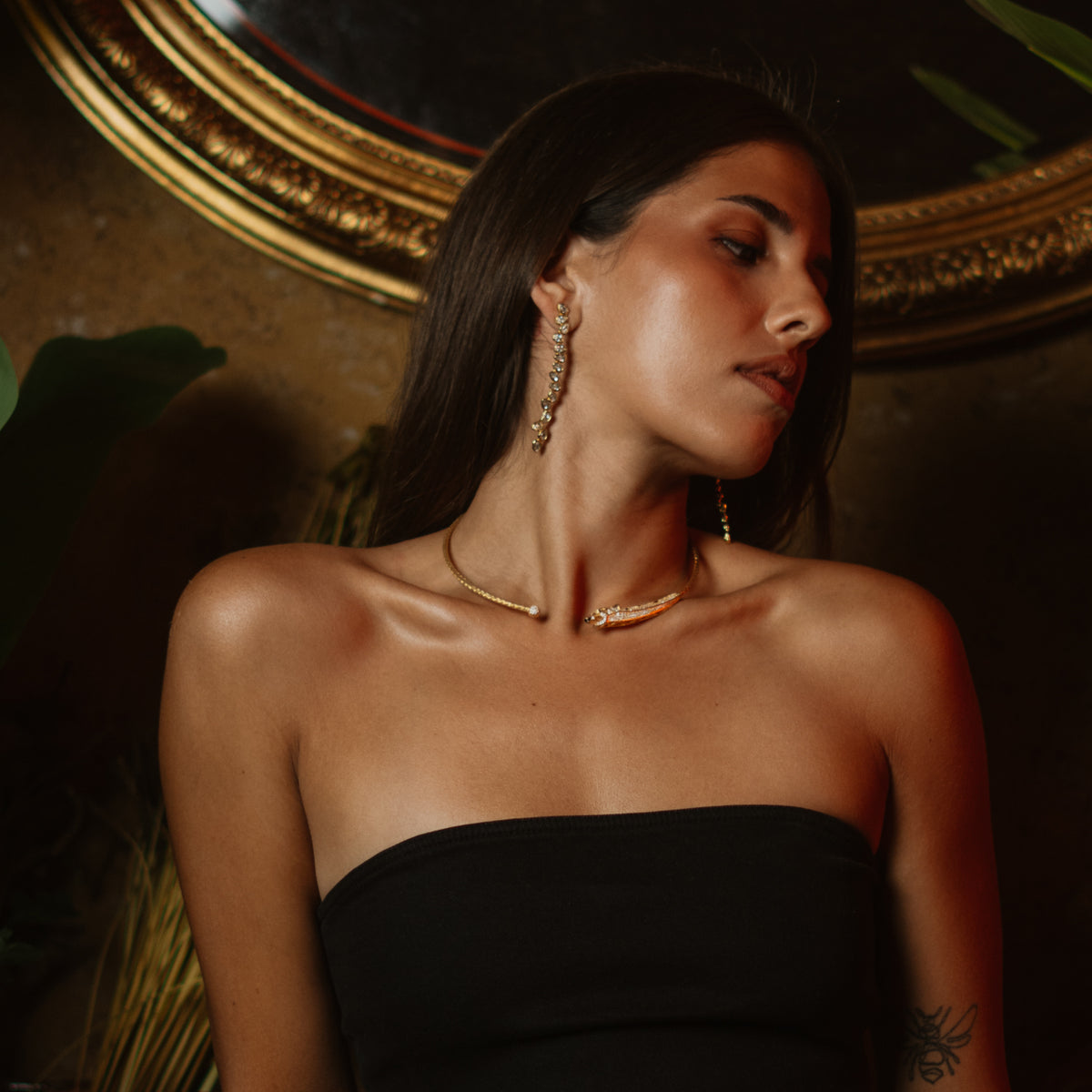 Model before a gilded mirror wearing the diamond vine long gold drop earrings and a panther collar