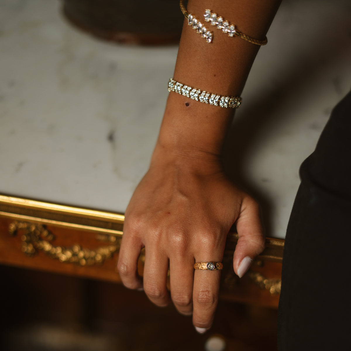 The Antique Ember band ring worn on the hand with gold tennis and cuff bracelets against a gilded mirror
