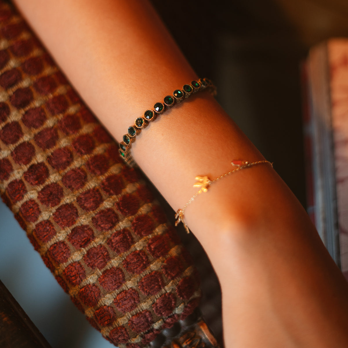The emerald tennis bracelet worn high on the forearm above a fine gold charm bracelet