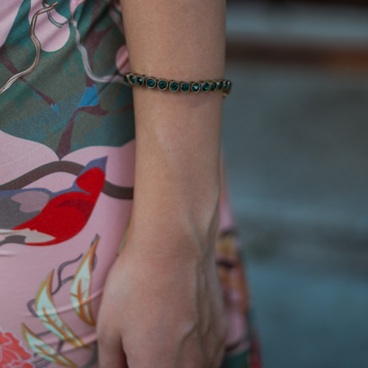The emerald green tennis bracelet worn on the wrist against a floral print dress