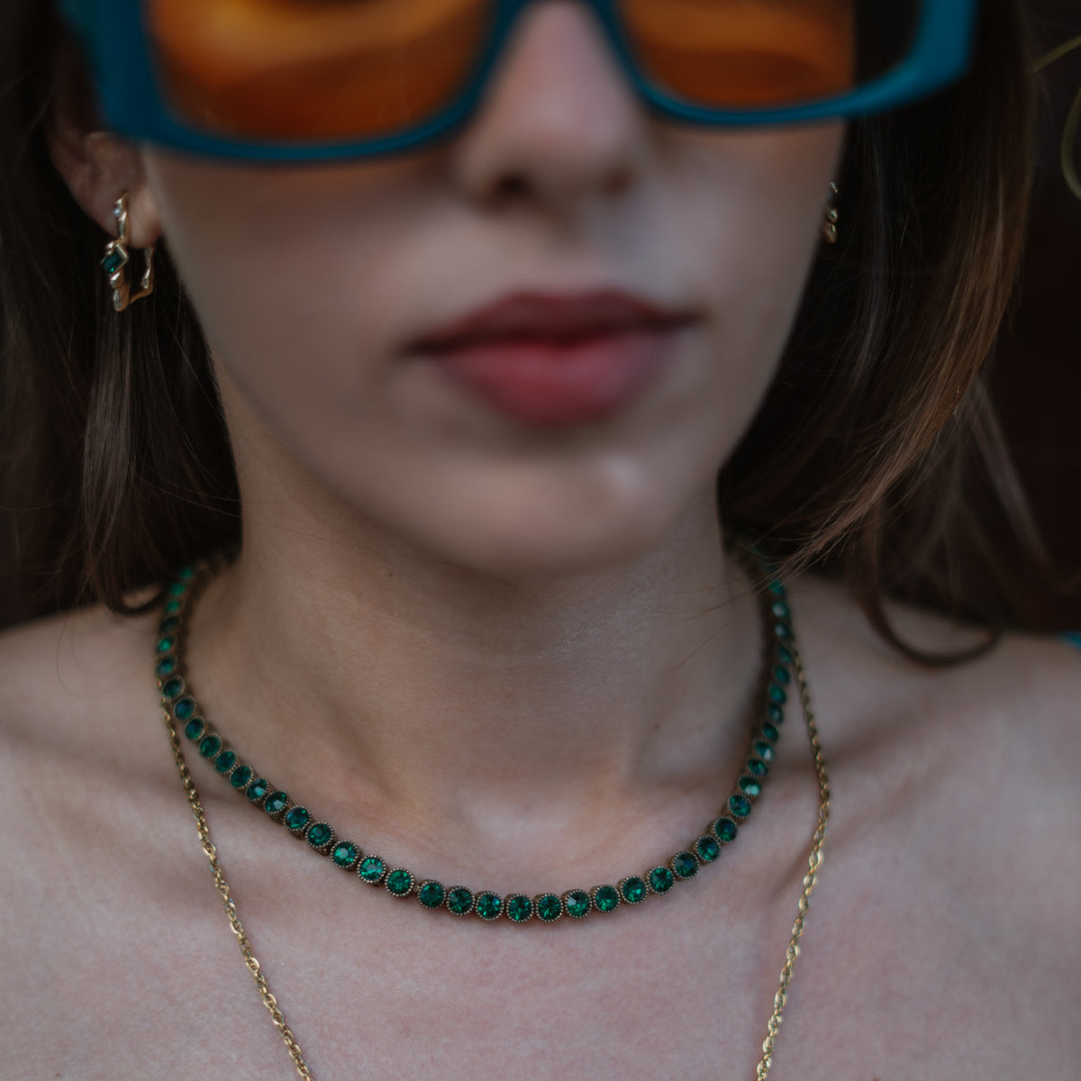 Detail of the emerald tennis necklace worn with matching green stone earrings and a fine gold chain