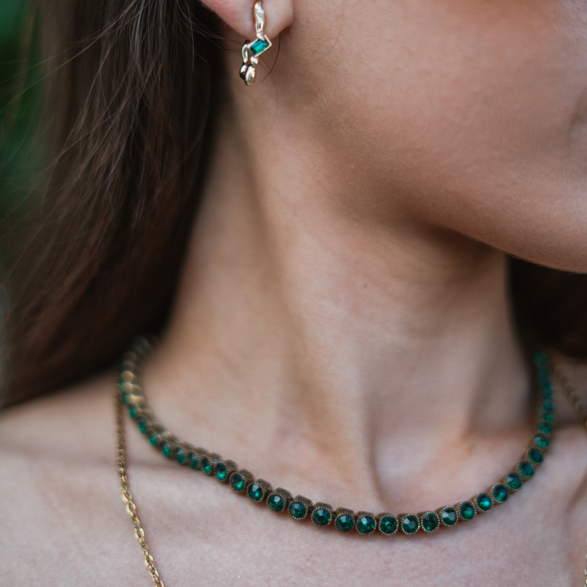 Close view of the emerald tennis necklace at the throat, each faceted green stone seated in its own patterned bezel