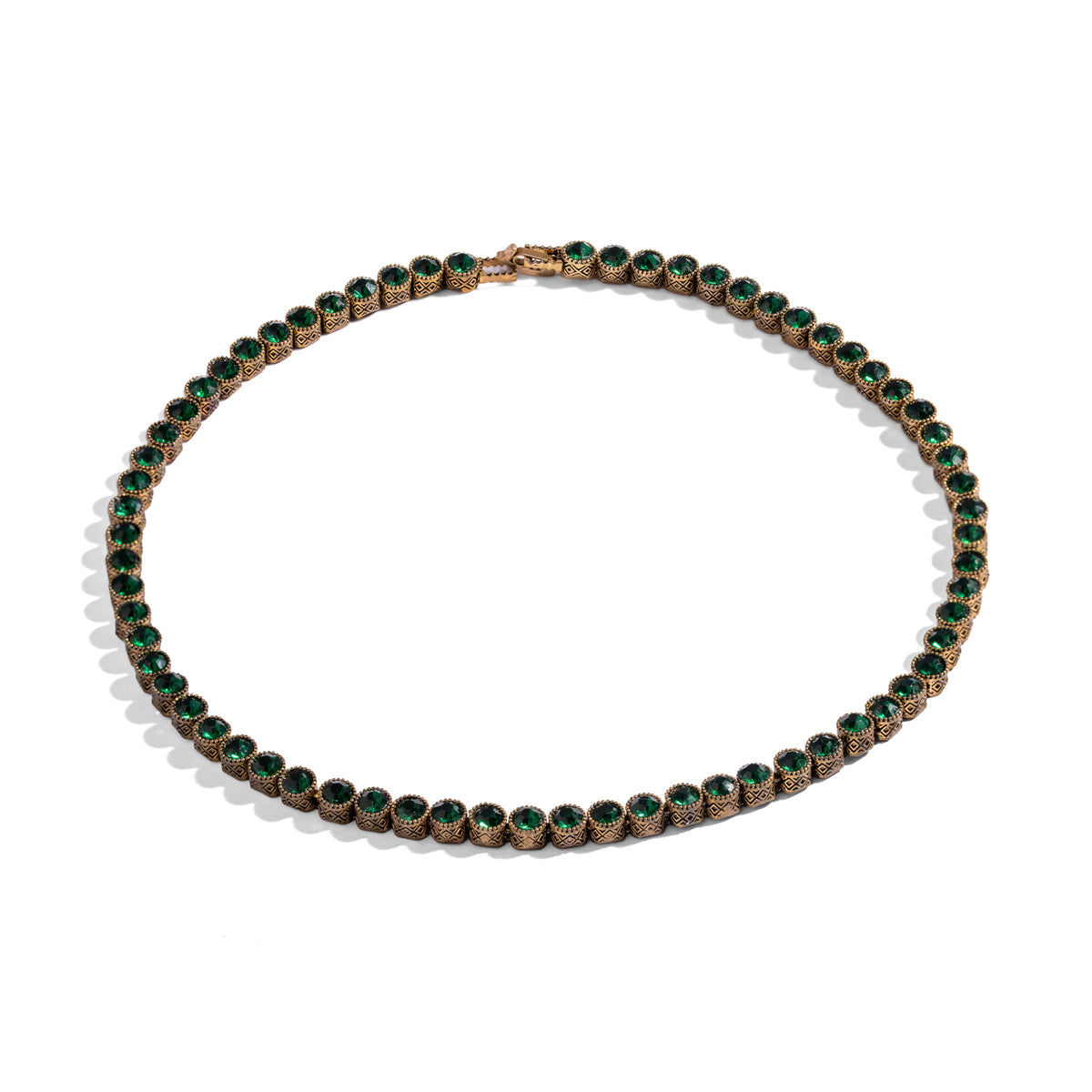 Overhead studio view of the emerald green tennis necklace, the darkened finish sitting in the recesses of each bezel