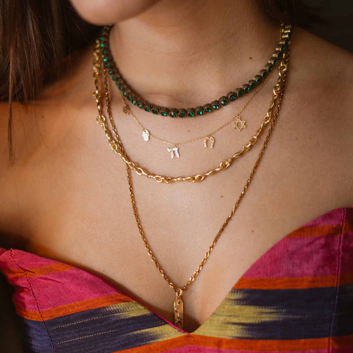 The emerald tennis necklace layered with a gold symbol charm necklace and a long gold pendant chain