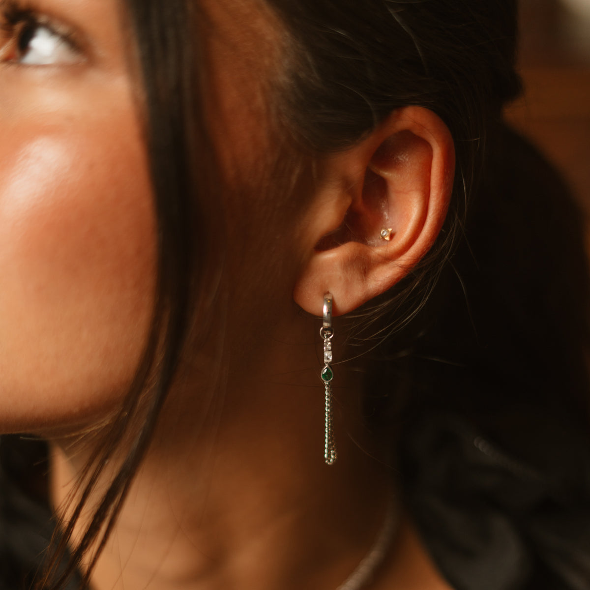 Emerald chain drape sterling silver huggie earring worn at the ear in warm evening light
